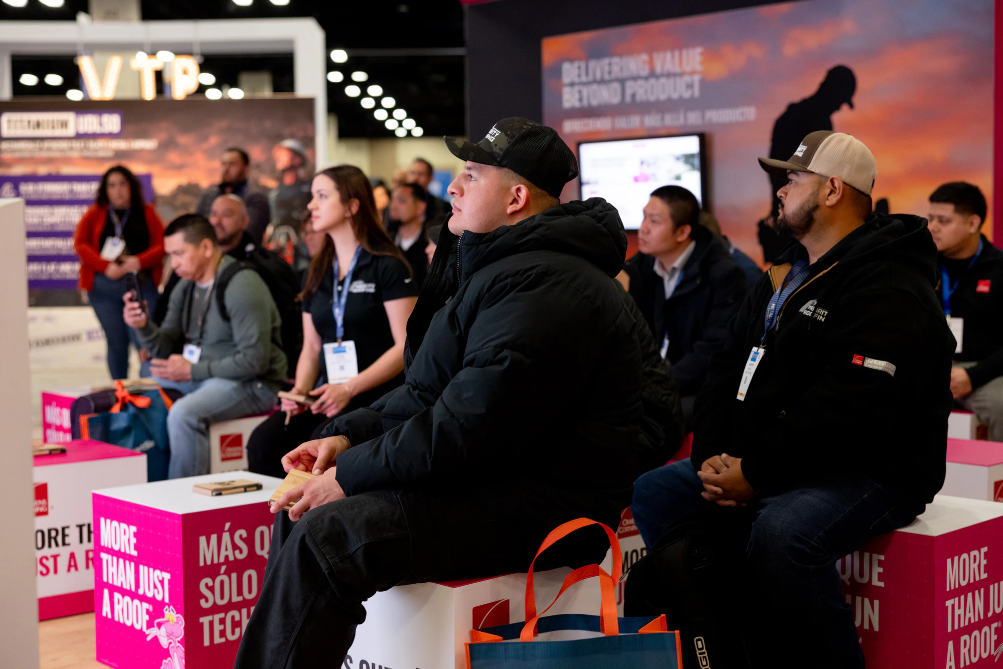 Contractors on the pink More Than Just a Roof cubes, listening to a Learning Lounge talk at Owens Corning at IRE 2025