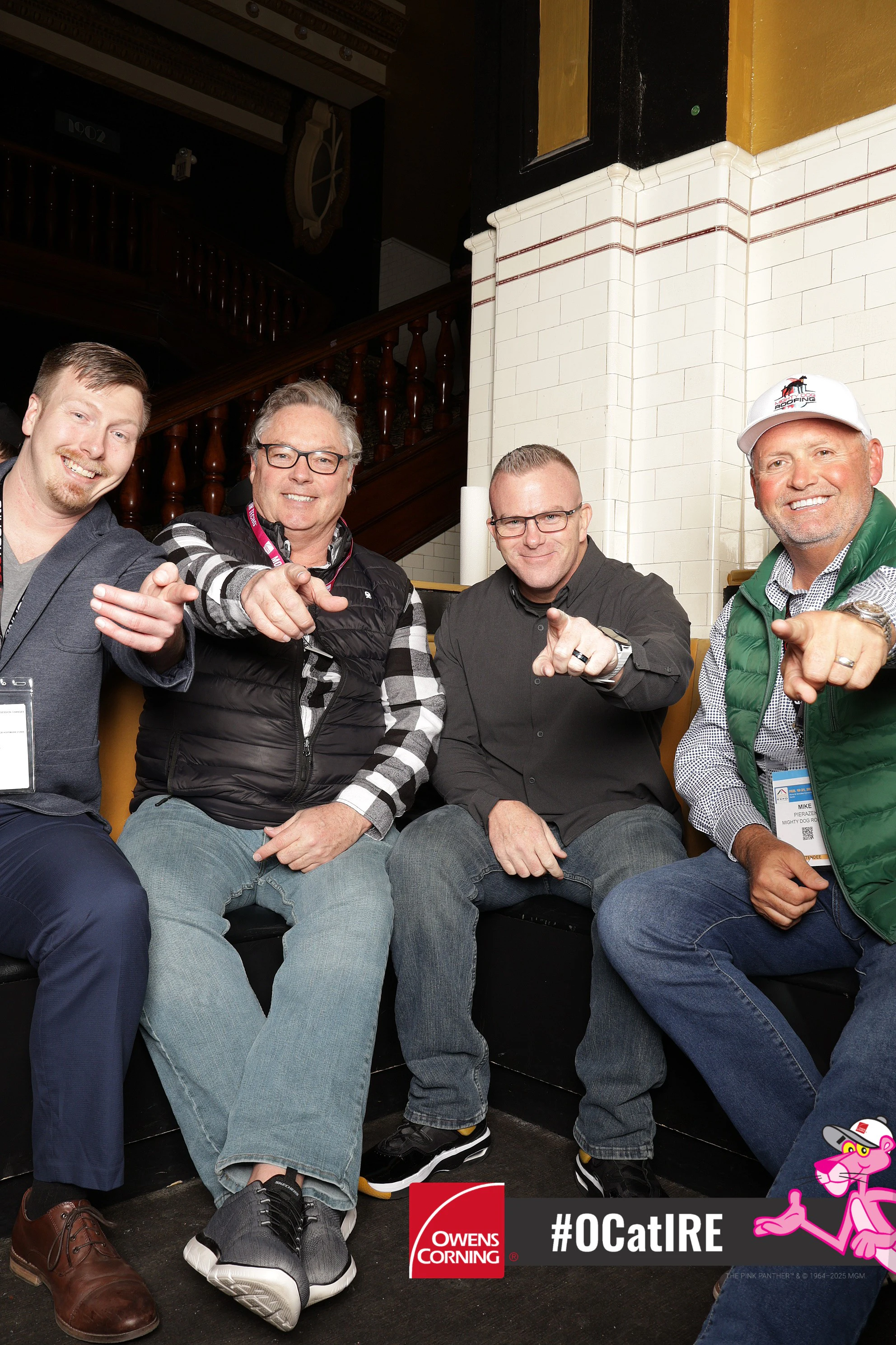 Four men on the booth bench pointing at the camera at Owens Corning at IRE 2025