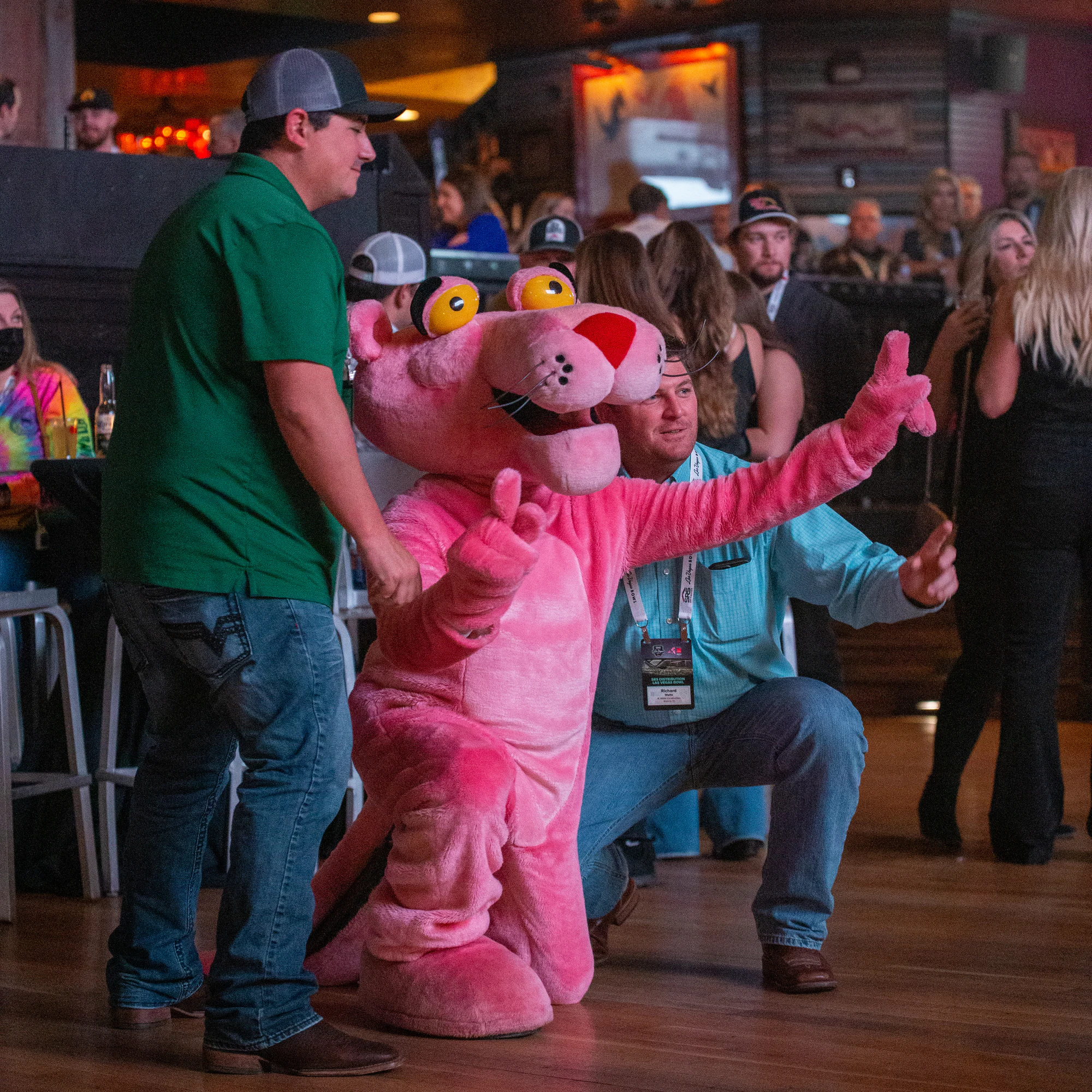 Pink Panther mascot and a kneeling guest both throw their arms out on the dance floor at Owens Corning at the 2021 Las Vegas Bowl