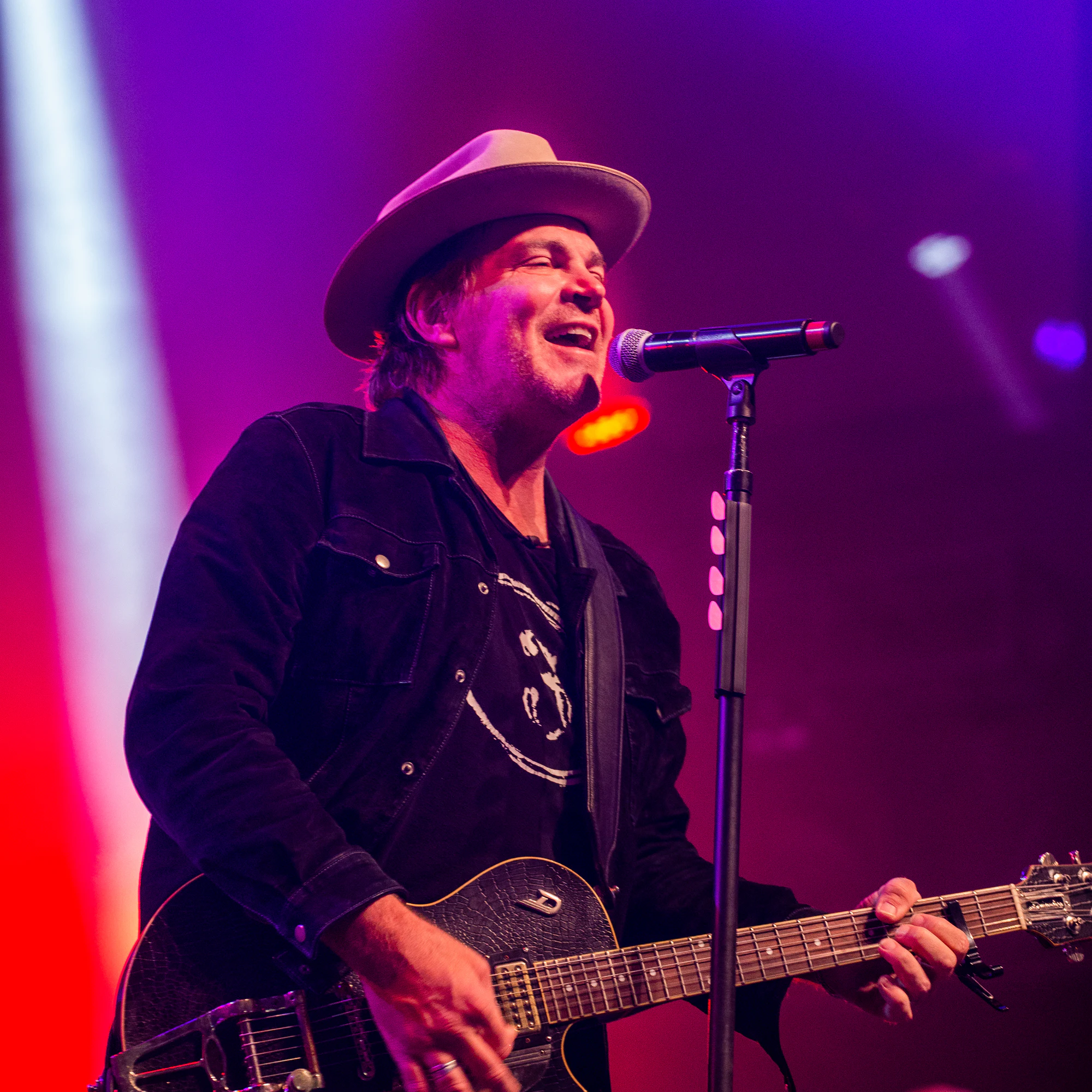 Singer in a hat laughing into the mic under pink stage light at Owens Corning at the 2021 Las Vegas Bowl