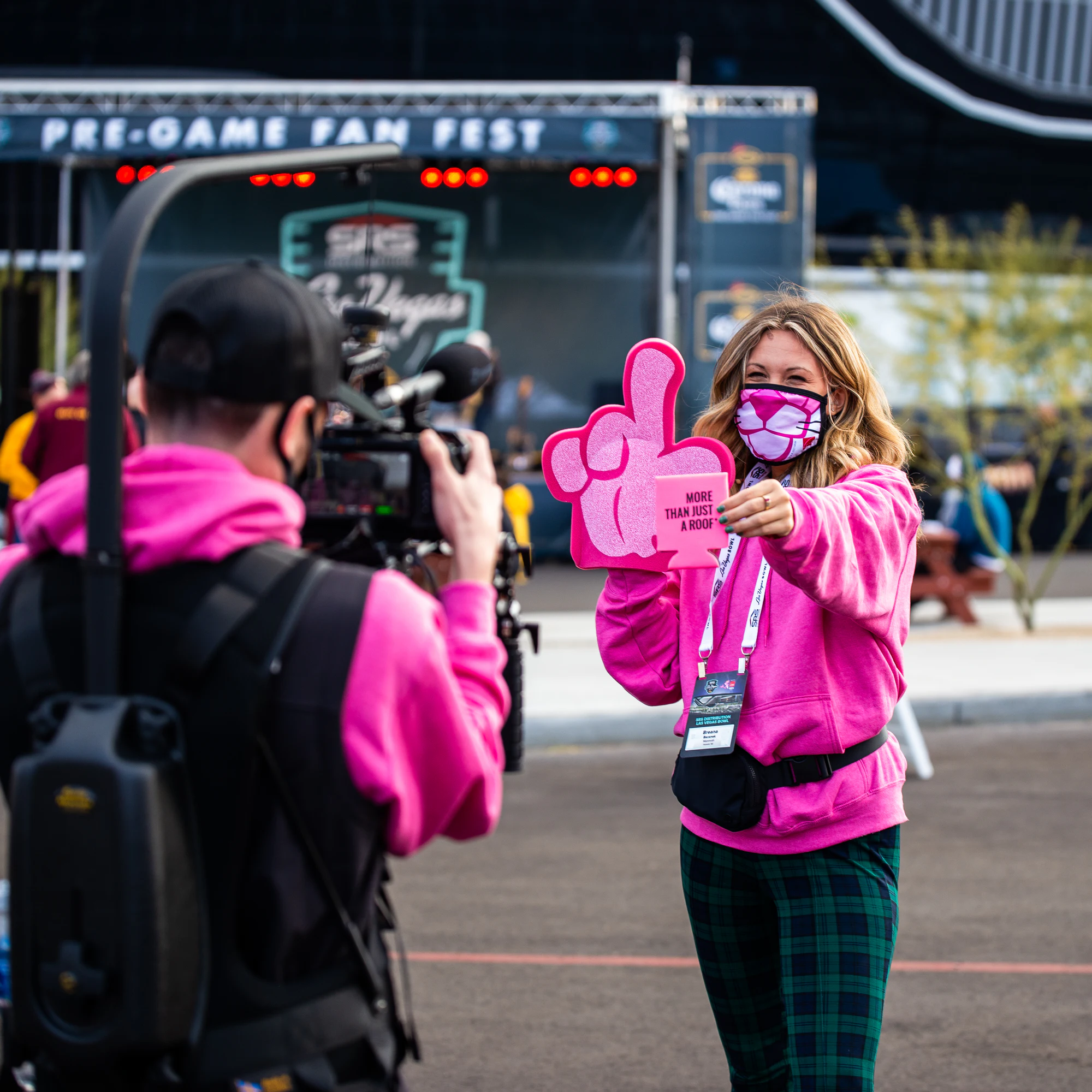 Camera operator in pink filming a woman with a foam hand under the Pre-Game Fan Fest sign at Owens Corning at the 2021 Las Vegas Bowl