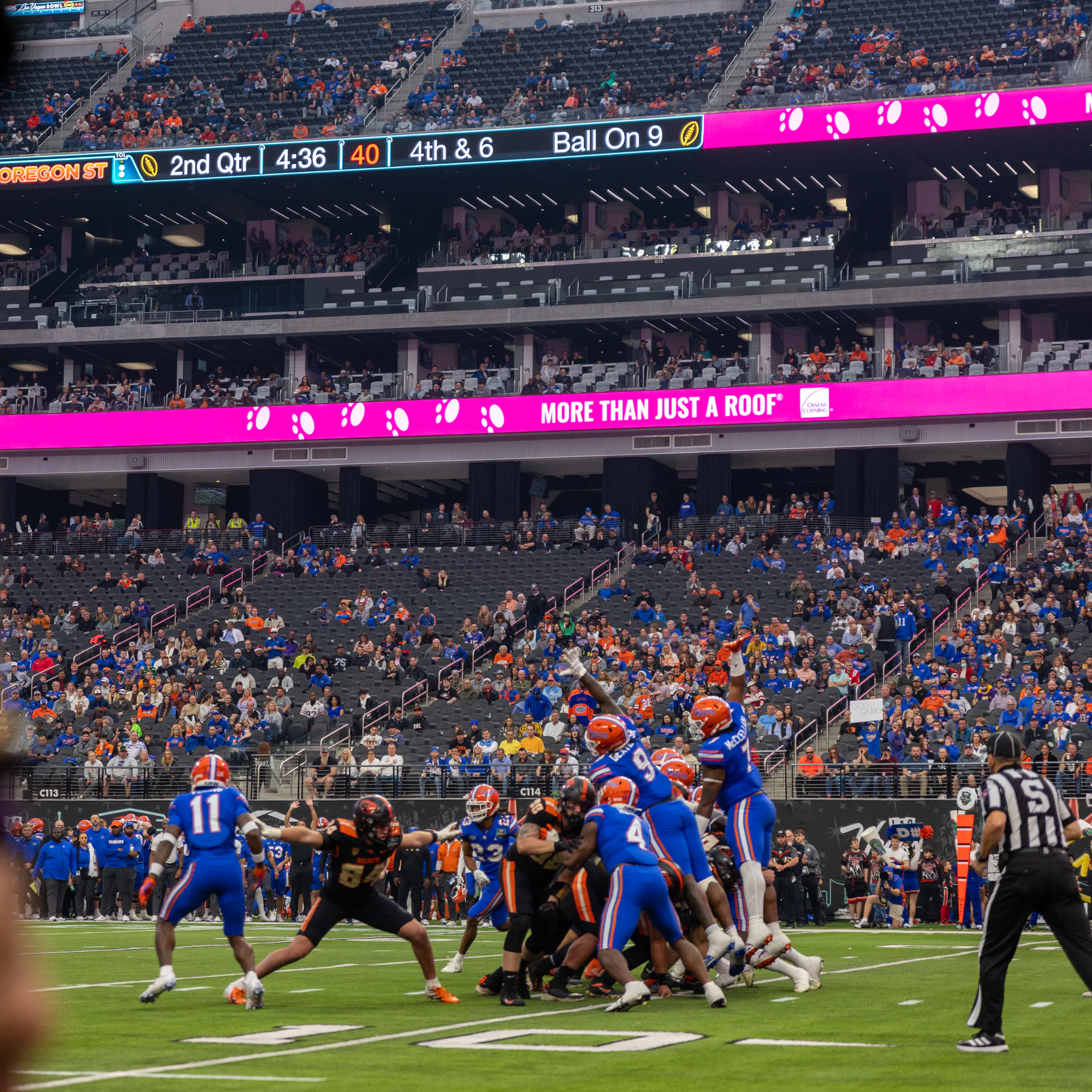 Game action on the field under a pink More Than Just A Roof ribbon board at Owens Corning at the 2022 Las Vegas Bowl