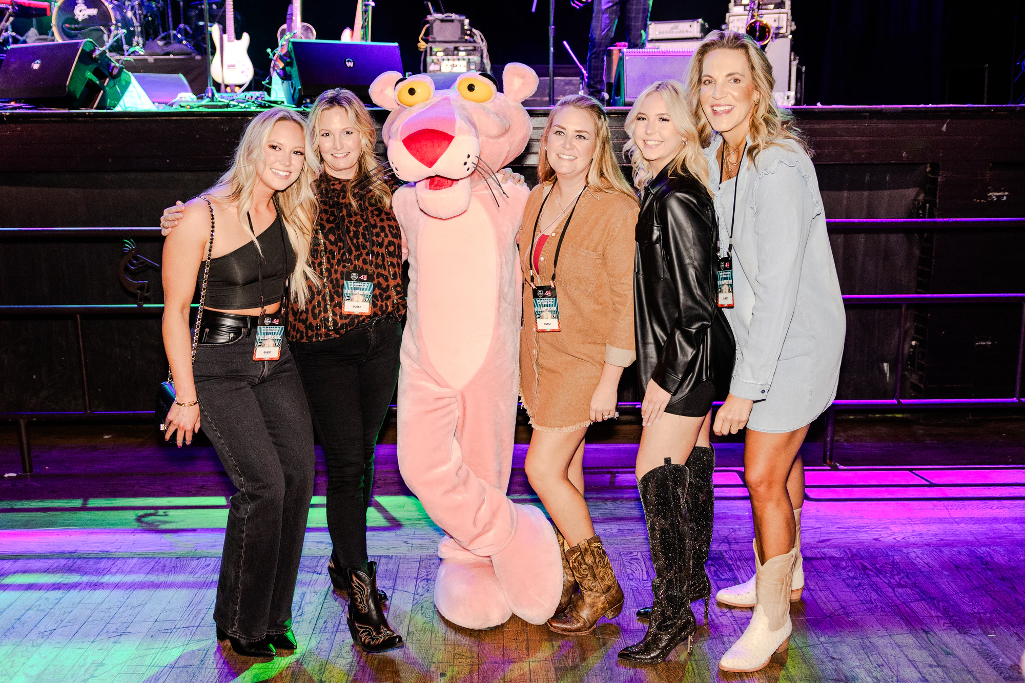 Five women on the concert dance floor with the Pink Panther, band gear on the stage behind at Owens Corning at the 2023 Las Vegas Bowl