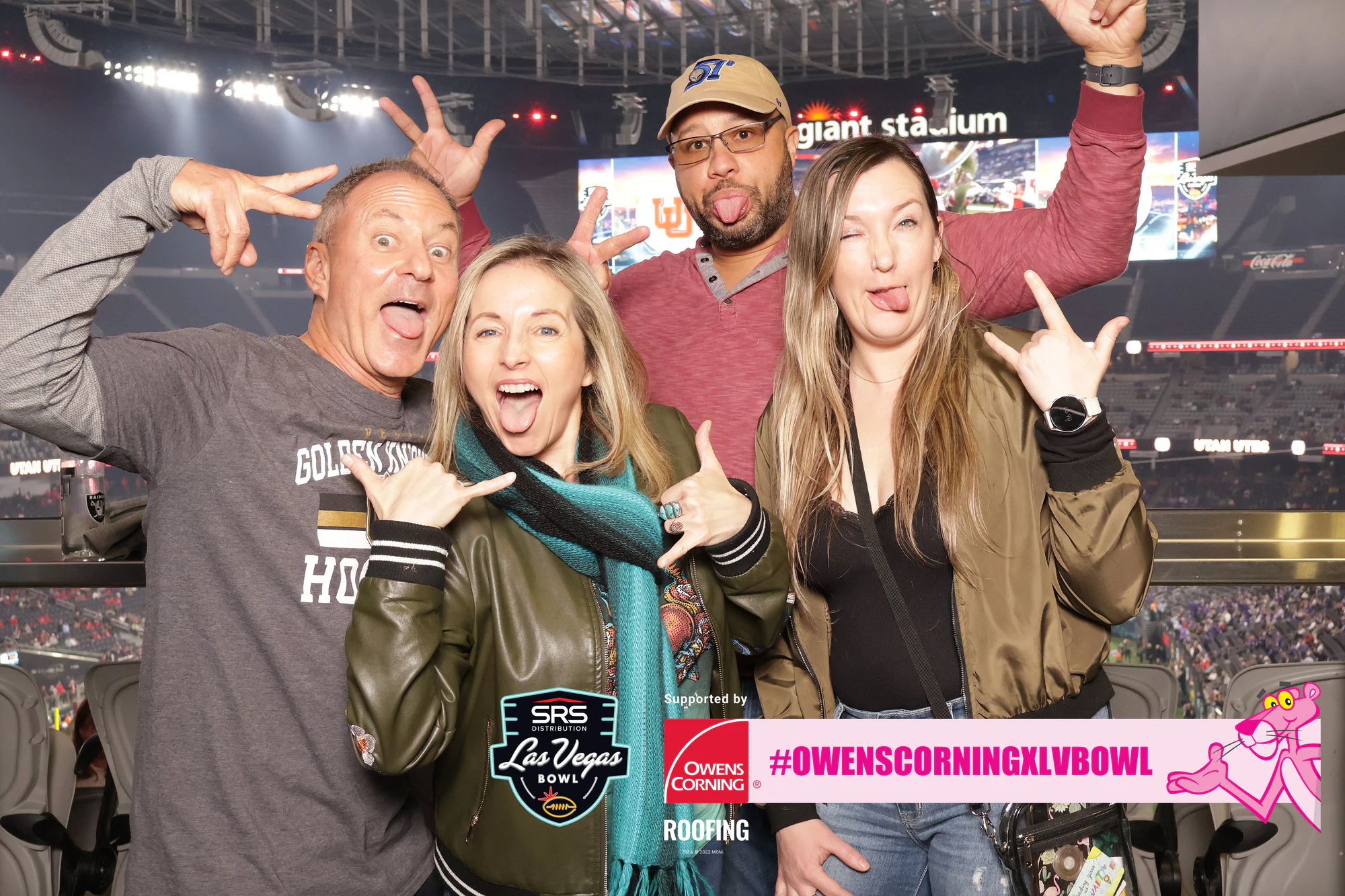 Four friends throwing hand signs in the suite, Allegiant Stadium lights and field behind at Owens Corning at the 2023 Las Vegas Bowl
