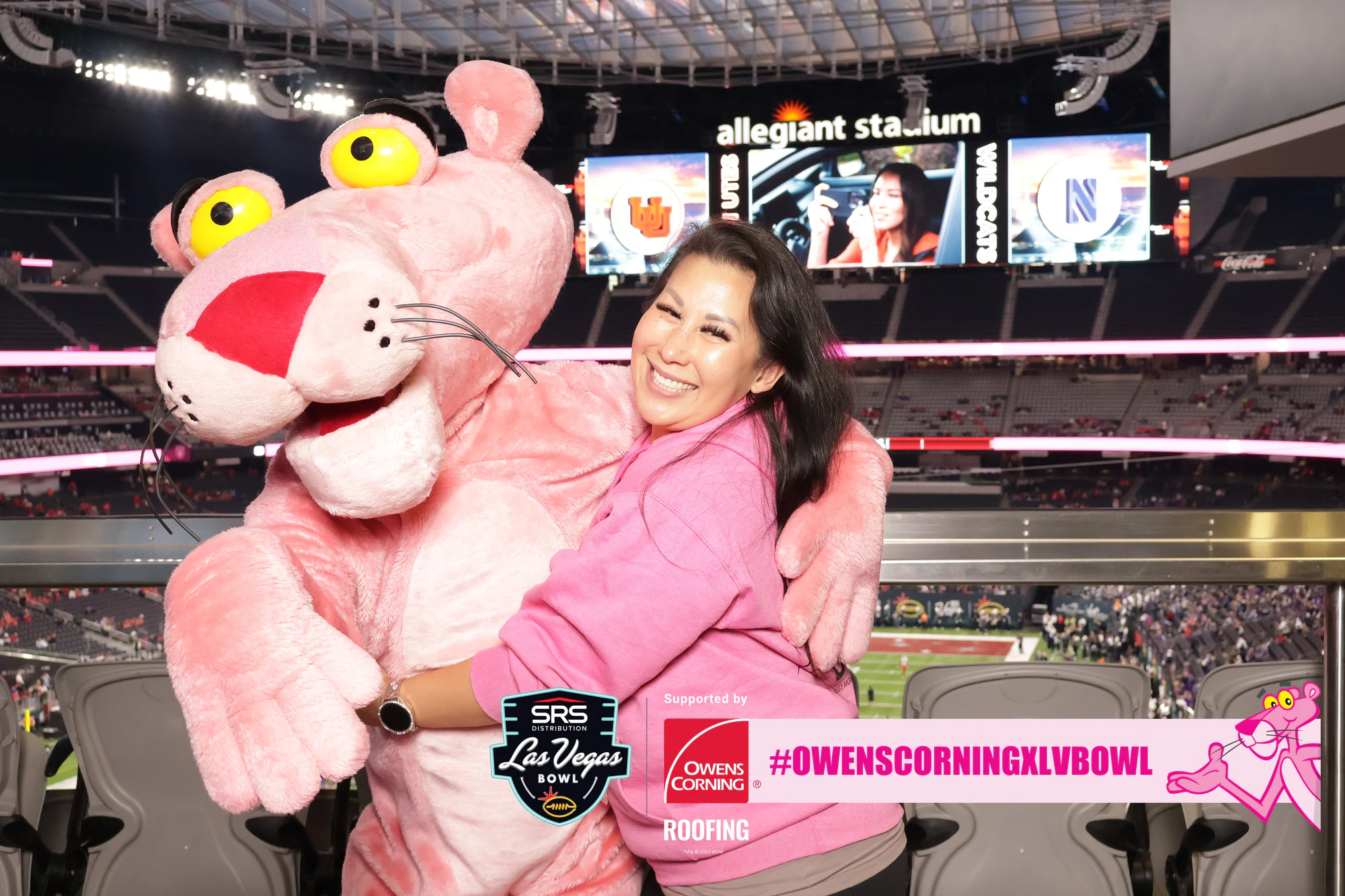 Woman in pink wraps the Pink Panther mascot in a hug, Allegiant Stadium sign behind at Owens Corning at the 2023 Las Vegas Bowl