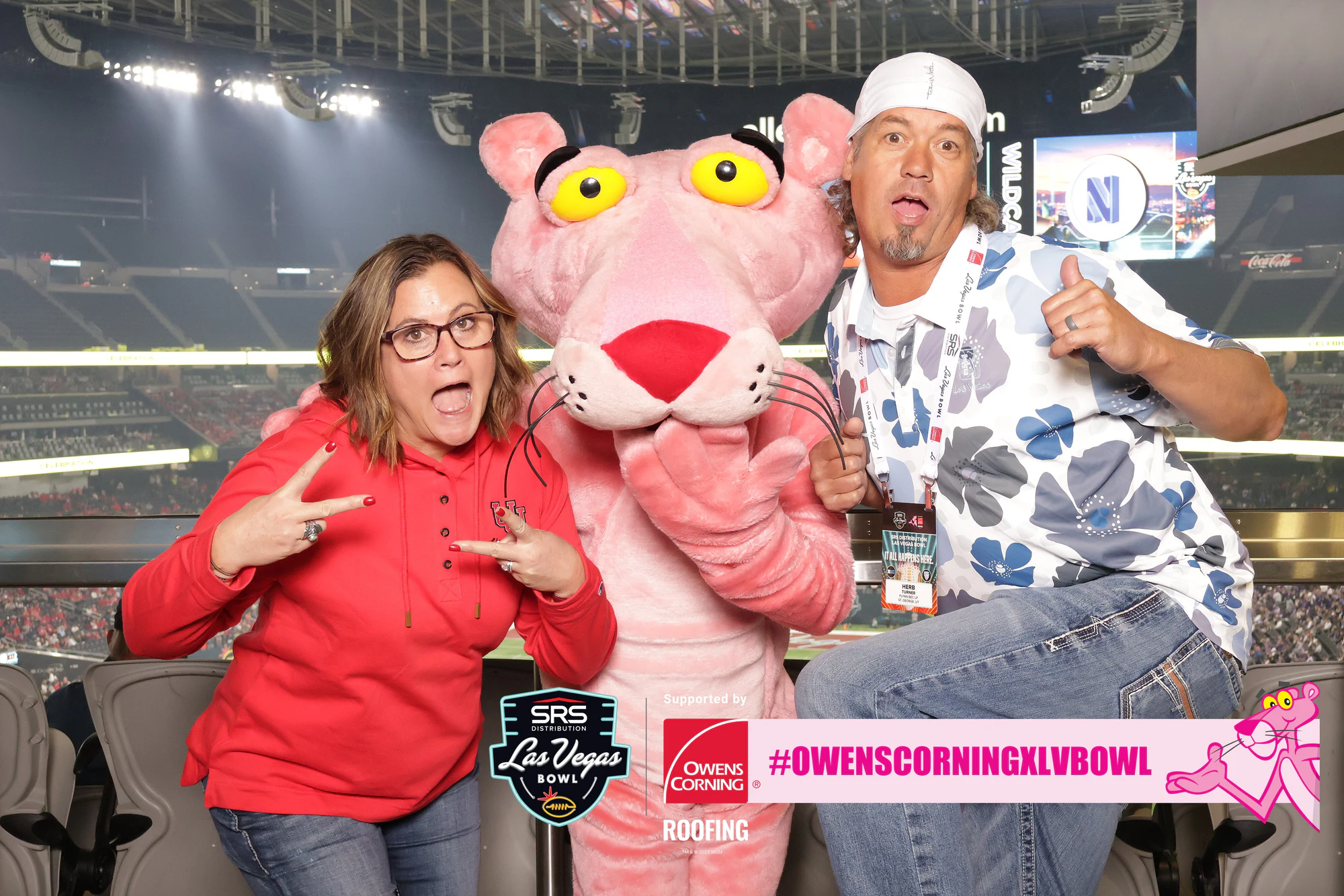 Two guests clowning around the Pink Panther mascot in the suite, stadium lights behind at Owens Corning at the 2023 Las Vegas Bowl