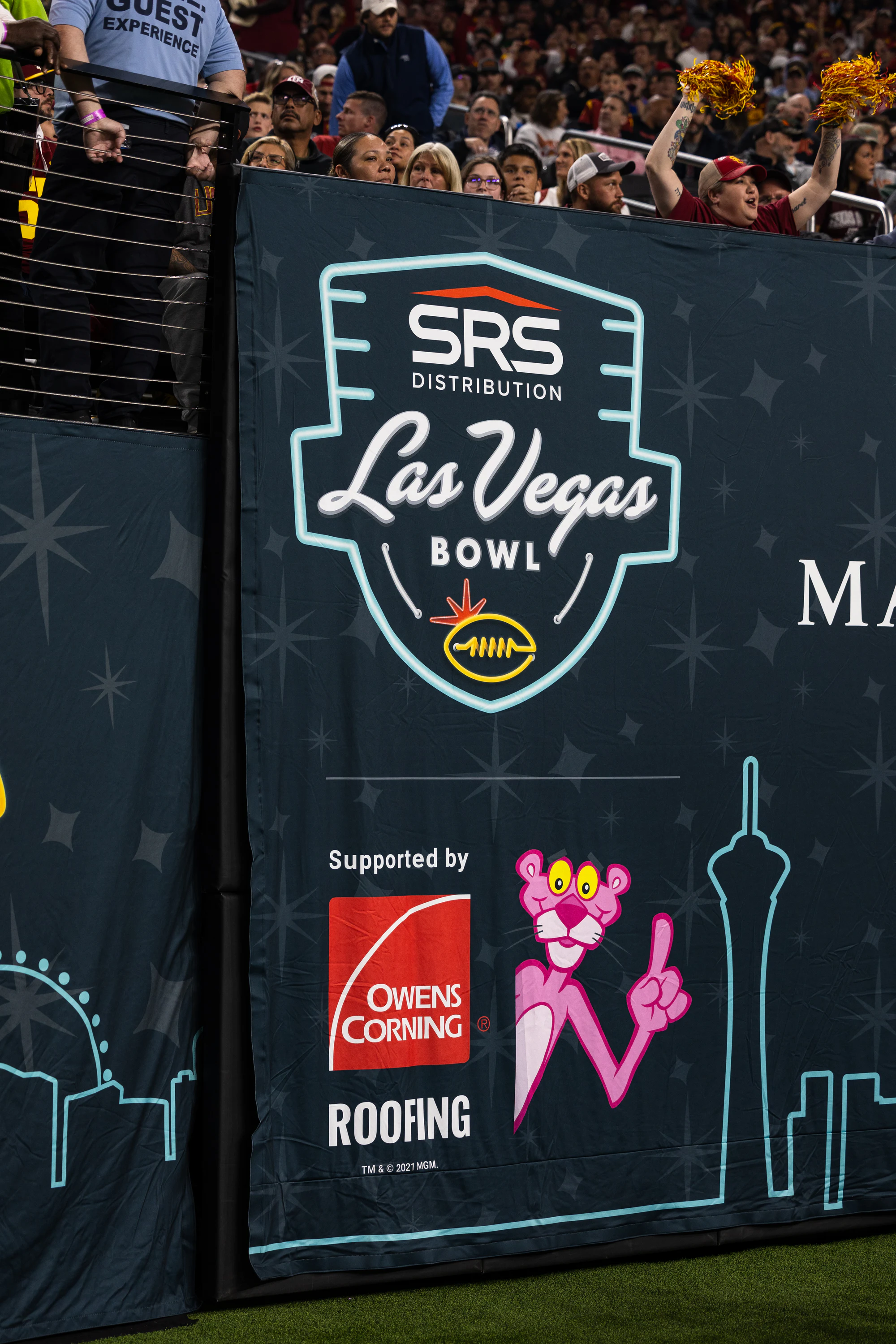 The Las Vegas Bowl wall sign reading Supported by Owens Corning Roofing, with the Pink Panther, fans leaning over it at Owens Corning at the 2024 Las Vegas Bowl