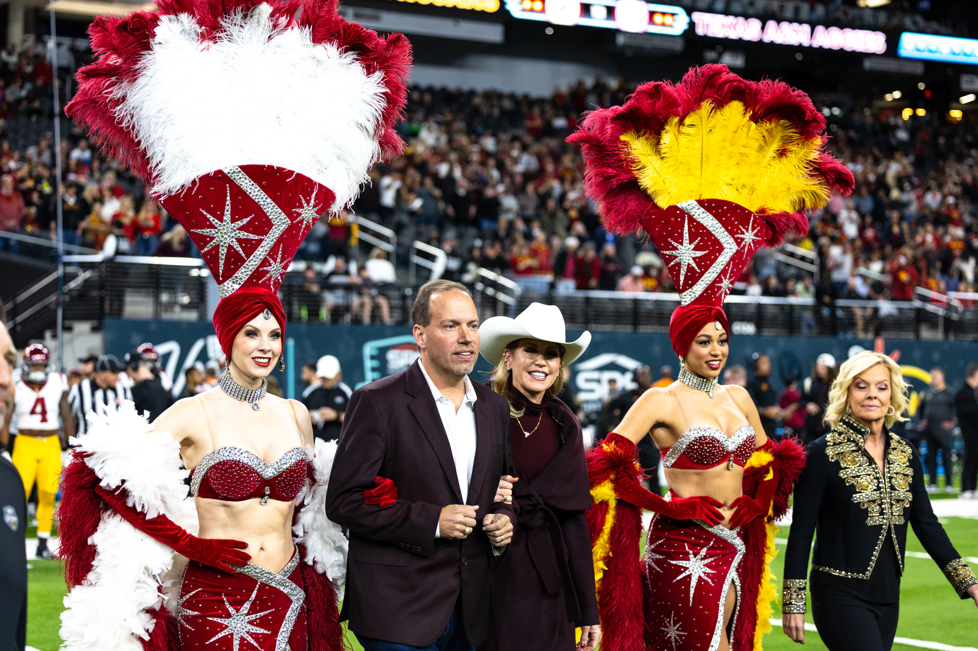 Showgirls in red feather headdresses walk the coin toss party onto the field at Owens Corning at the 2024 Las Vegas Bowl