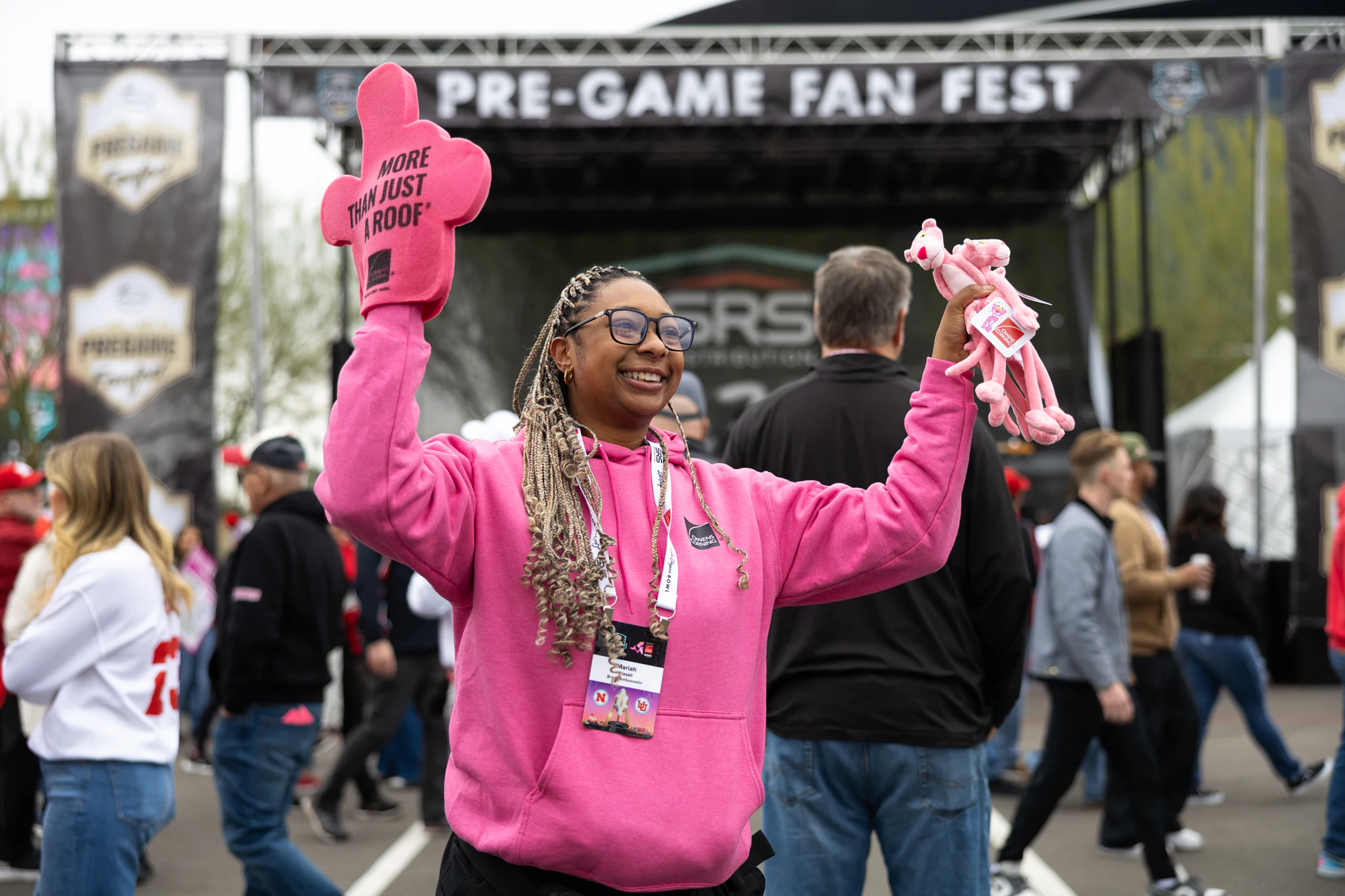 Woman in a pink hoodie waving a pink foam finger in front of the Pre-Game Fan Fest stage at Owens Corning at the 2025 Las Vegas Bowl
