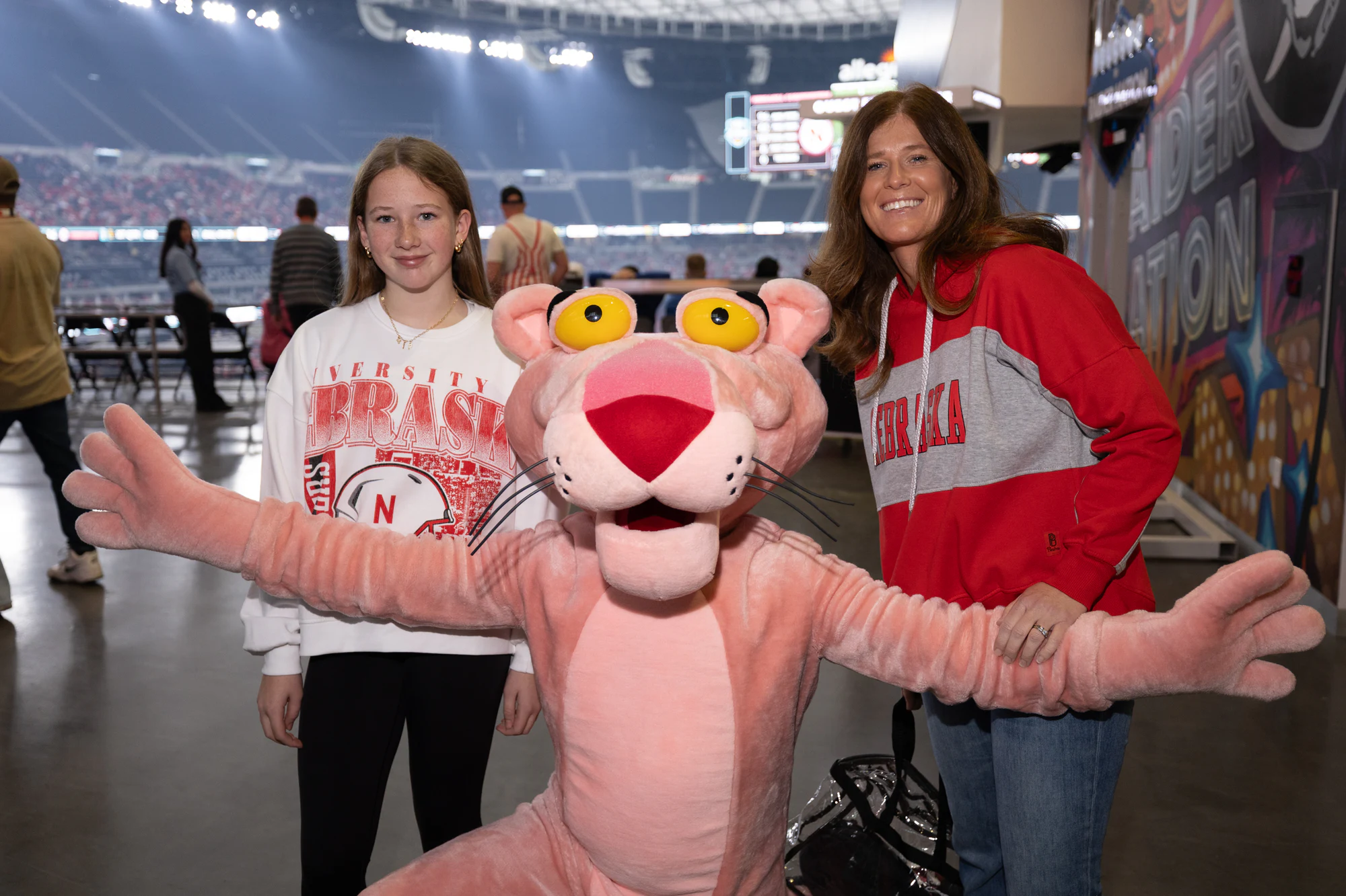 Panther spreading its arms in front of two Nebraska fans on the concourse at Owens Corning at the 2025 Las Vegas Bowl