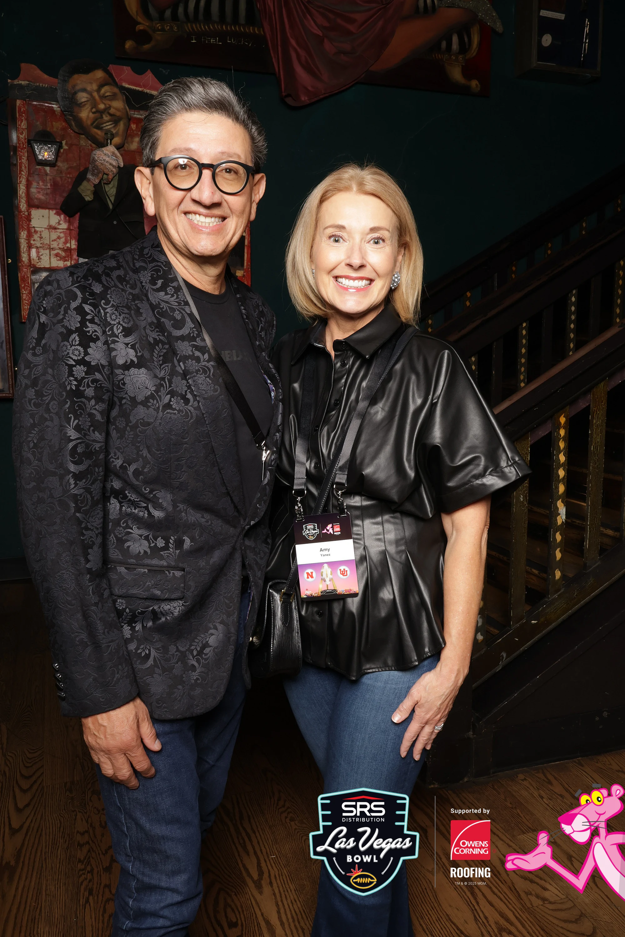 A man in glasses and a patterned black jacket with a woman in a black leather top at the concert booth at Owens Corning at the 2025 Las Vegas Bowl