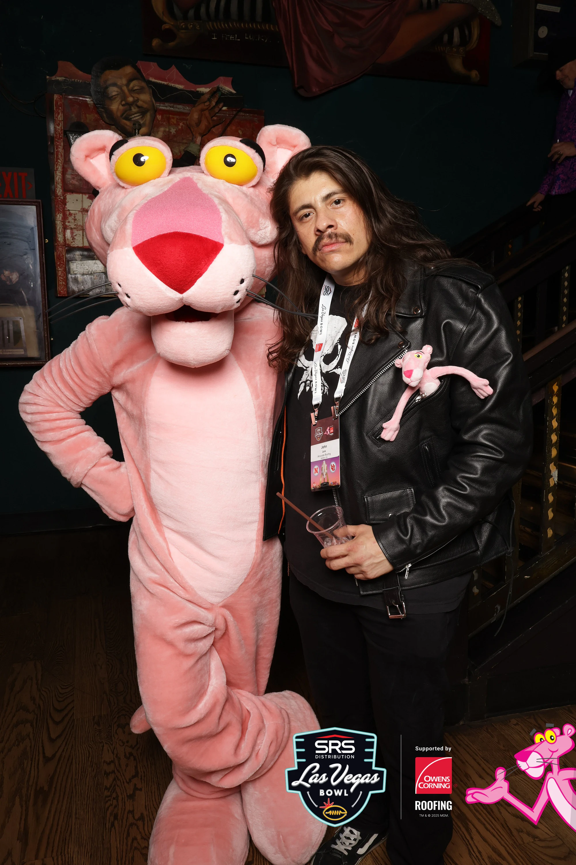 The Pink Panther posing beside a guest with long hair in a black leather jacket at Owens Corning at the 2025 Las Vegas Bowl