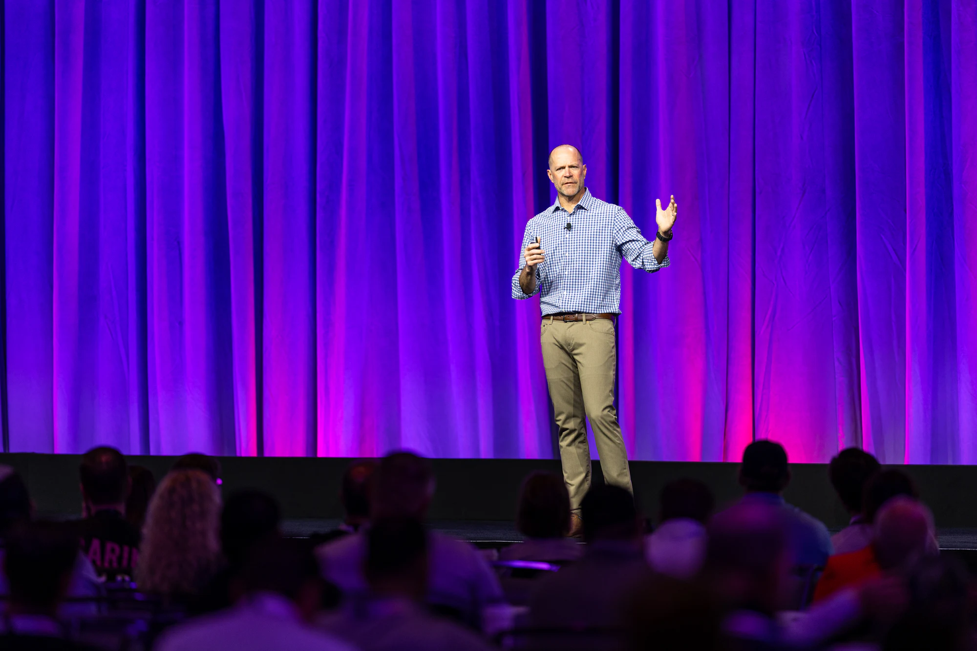 A keynote speaker on stage in front of a purple-lit curtain, the audience in the foreground, at the Owens Corning Platinum Conference 2025