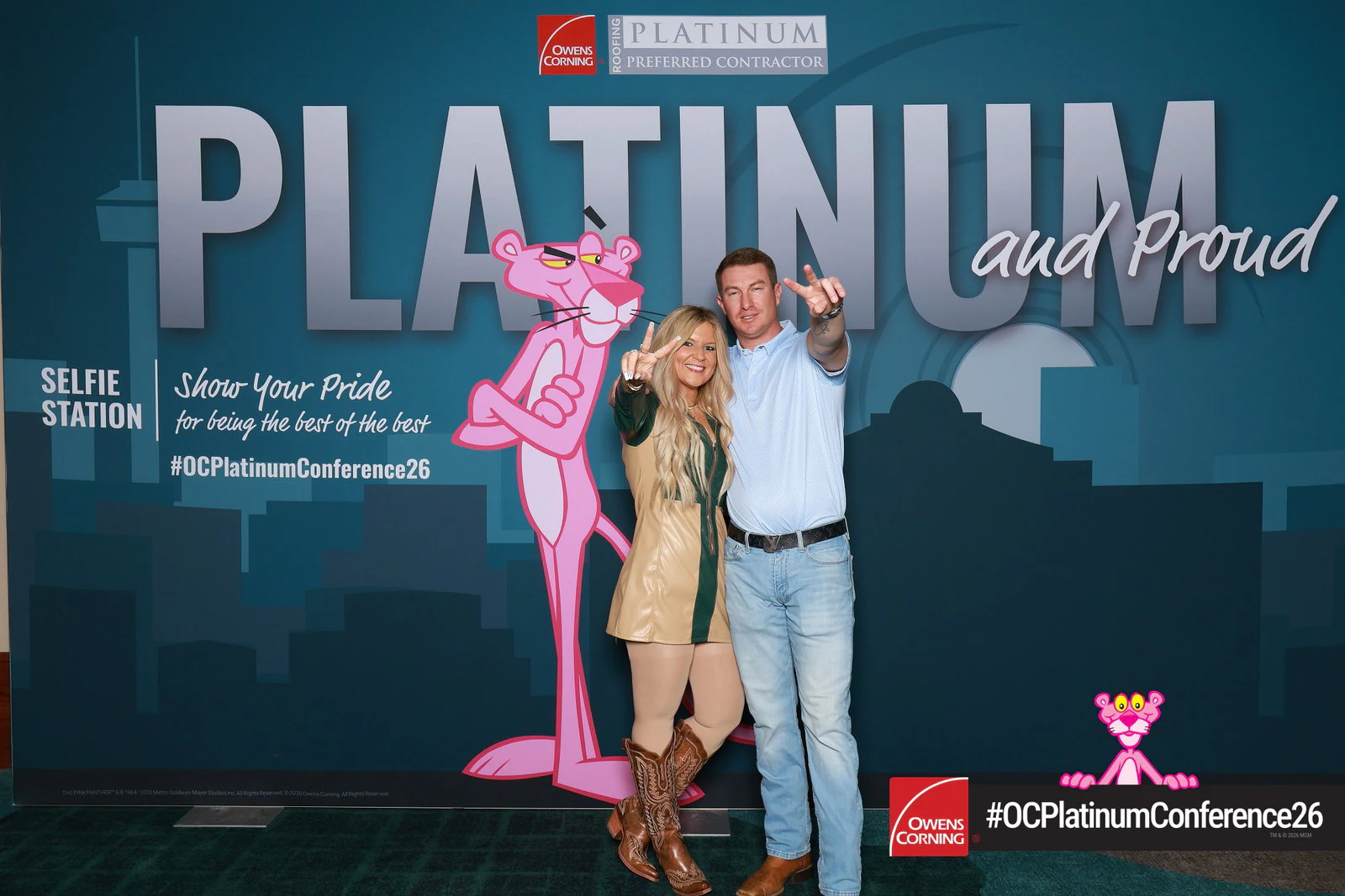 A woman in a tan dress and cowboy boots throwing a peace sign beside a man in a blue shirt pointing at the camera at Owens Corning Platinum Conference 2026