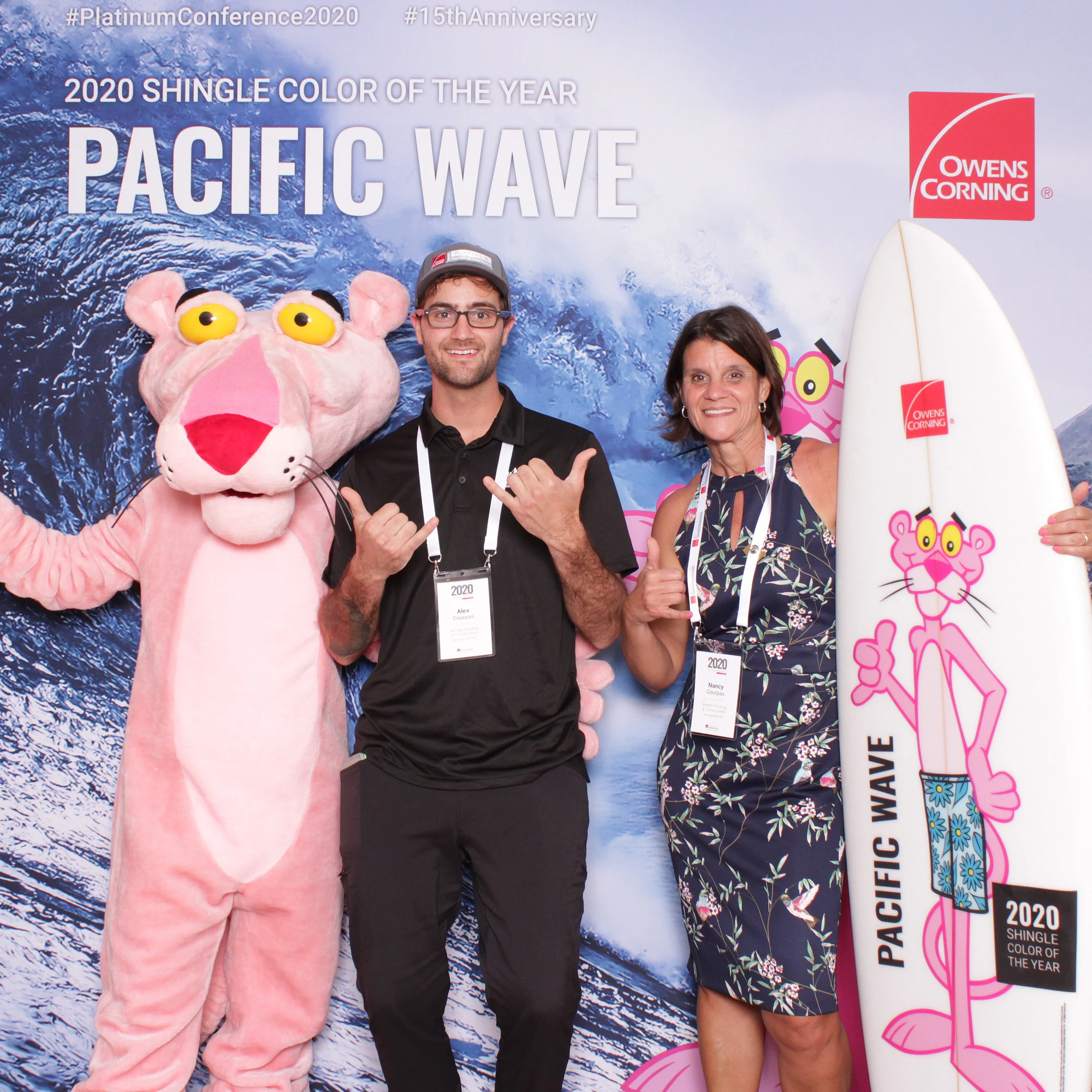 A man in a cap and a woman in a navy floral dress with the Pink Panther and a white Pacific Wave surfboard at Owens Corning Platinum Conference