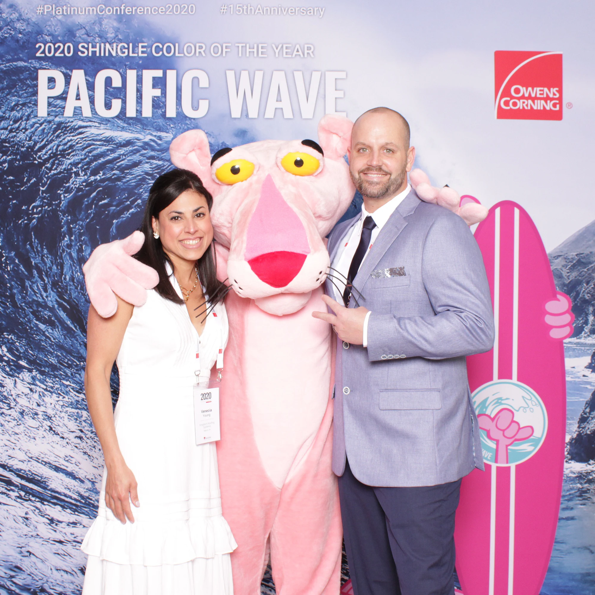 A woman in a white dress and a man in a gray suit with an arm around the Pink Panther at Owens Corning Platinum Conference
