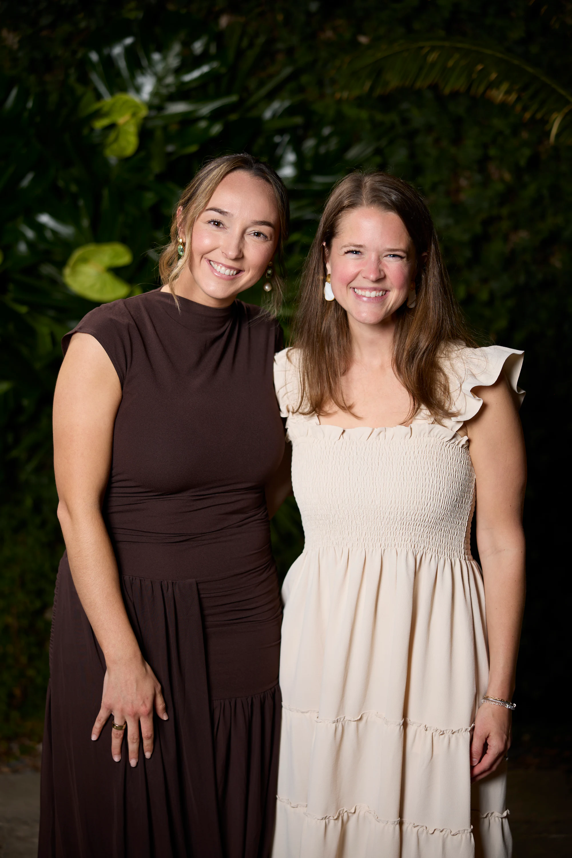 Two guests, one in a brown dress and one in a cream dress, in front of the plant wall at the Planterra Open House