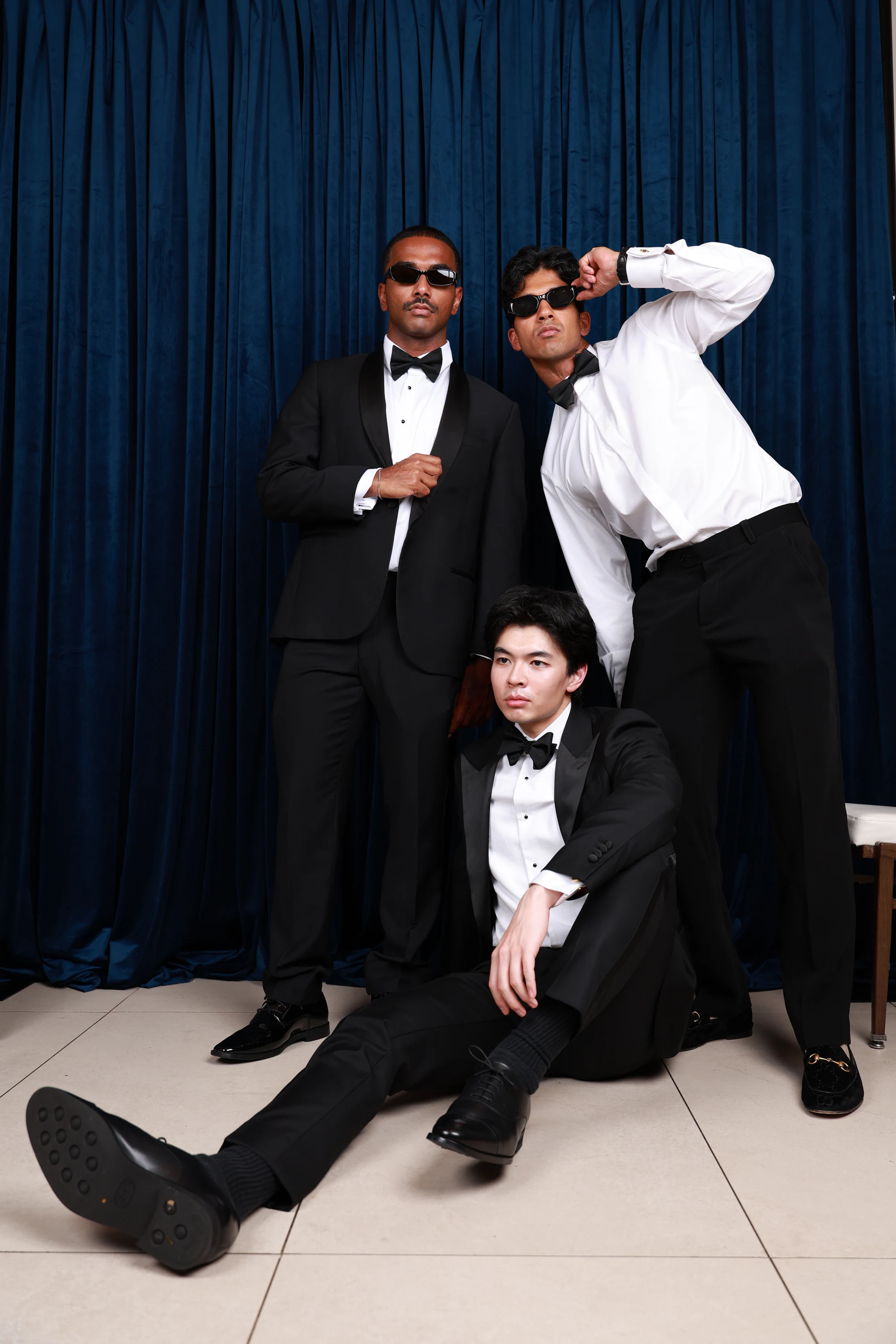 Three in tuxes with one stretched out across a chair at Ramya + Sreehari