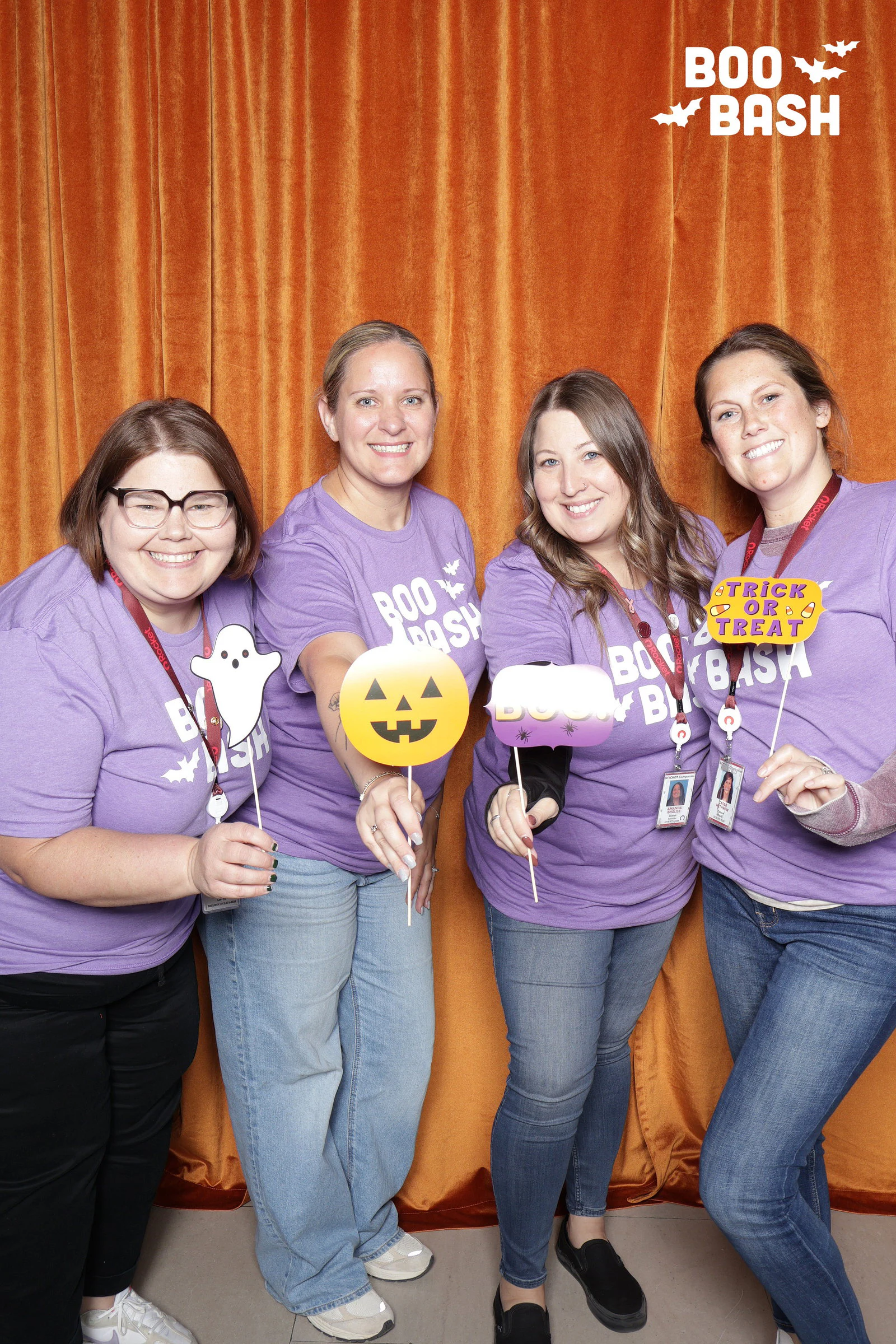 Four women in purple party T-shirts holding ghost, pumpkin and trick-or-treat props on sticks at Rocket Boo Bash