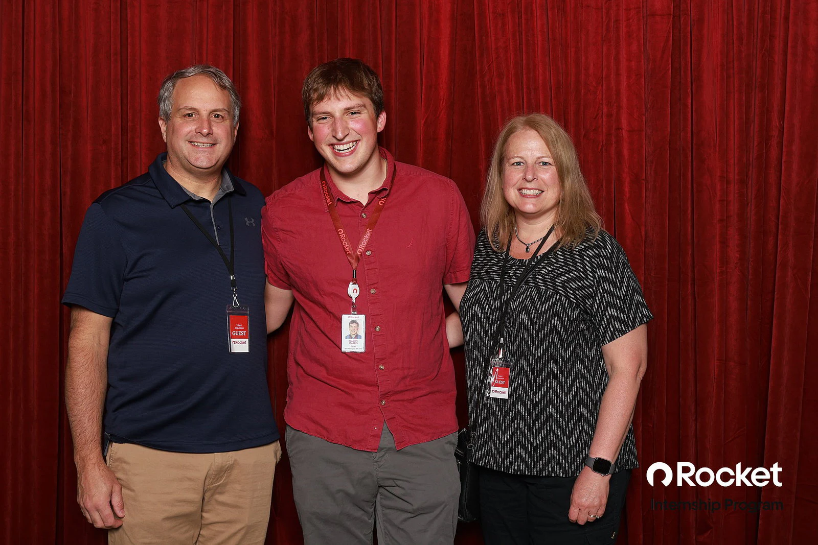 A man in a navy polo, a young man in a red shirt and a woman in a black and white top, shoulder to shoulder at Intern Open House with Rocket