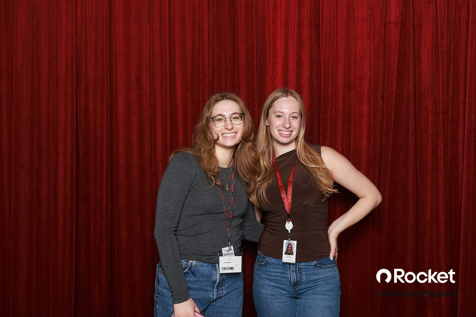 Two young women in jeans, one in glasses, standing close and smiling at Intern Open House with Rocket