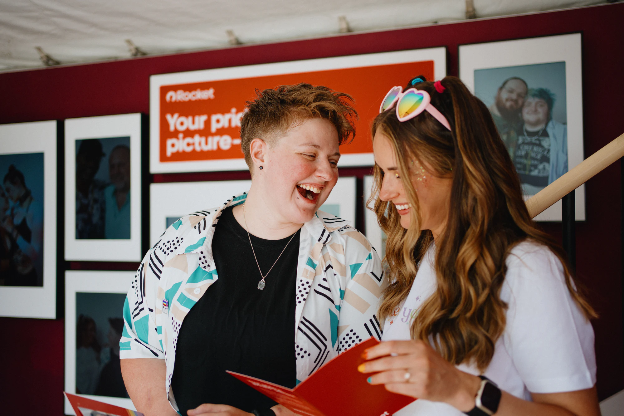 Two guests reading prints at the gallery wall at My Chosen Family Portraits at Motor City Pride 2025