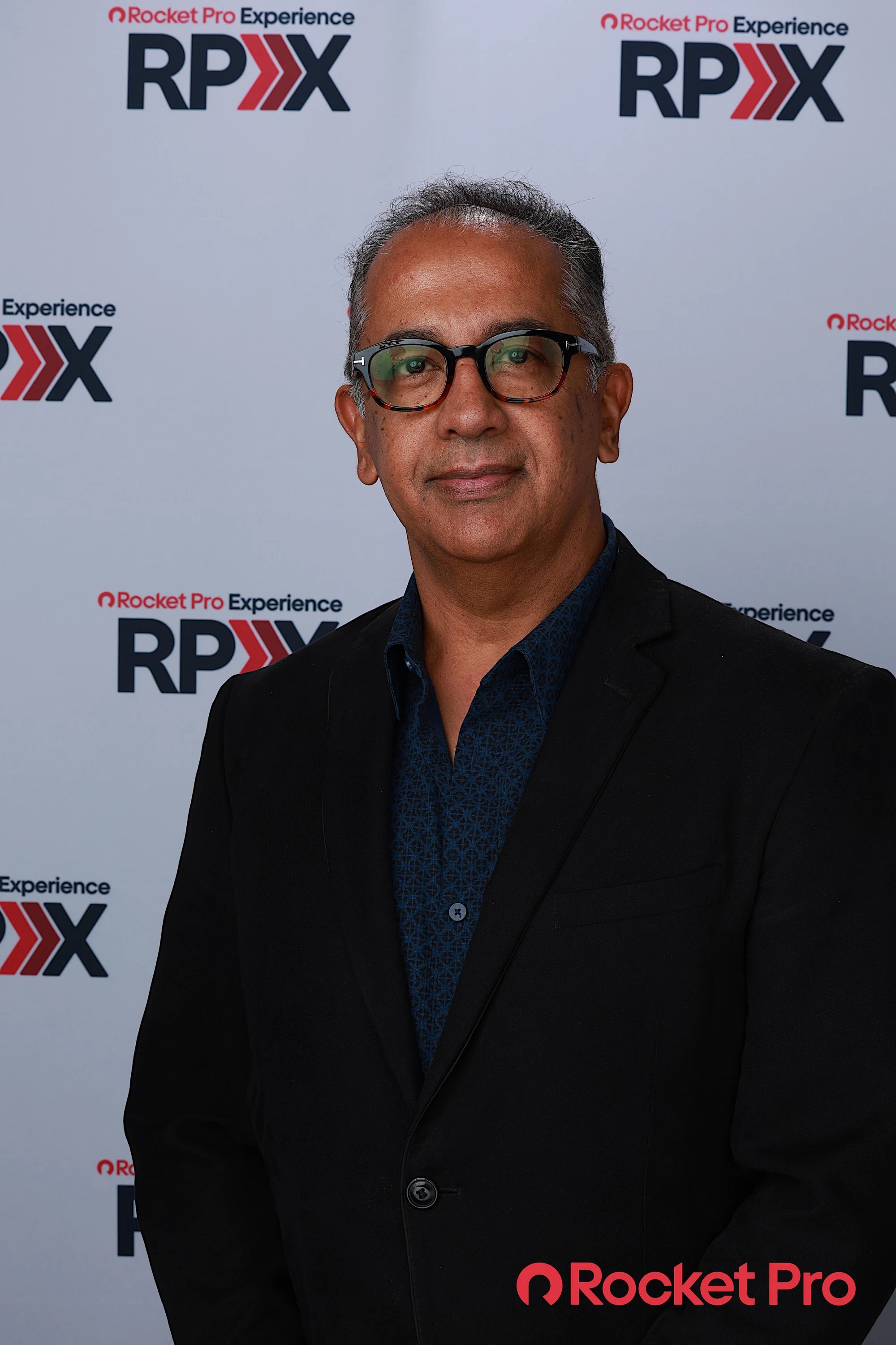 A man in glasses and a black blazer in front of the RPX wall at Rocket Pro Experience