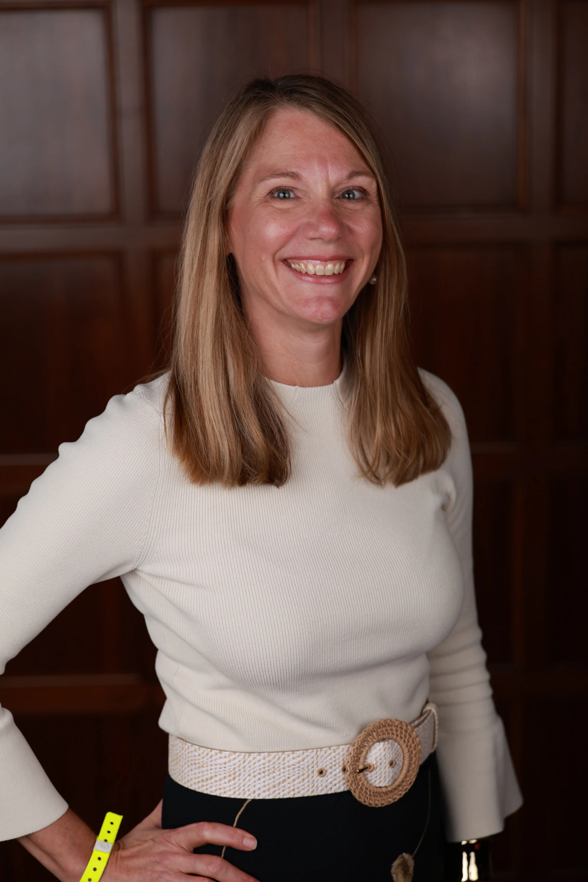 A woman in a cream sweater with a hand on her hip against a wood-paneled wall at Remote Welcome Reception