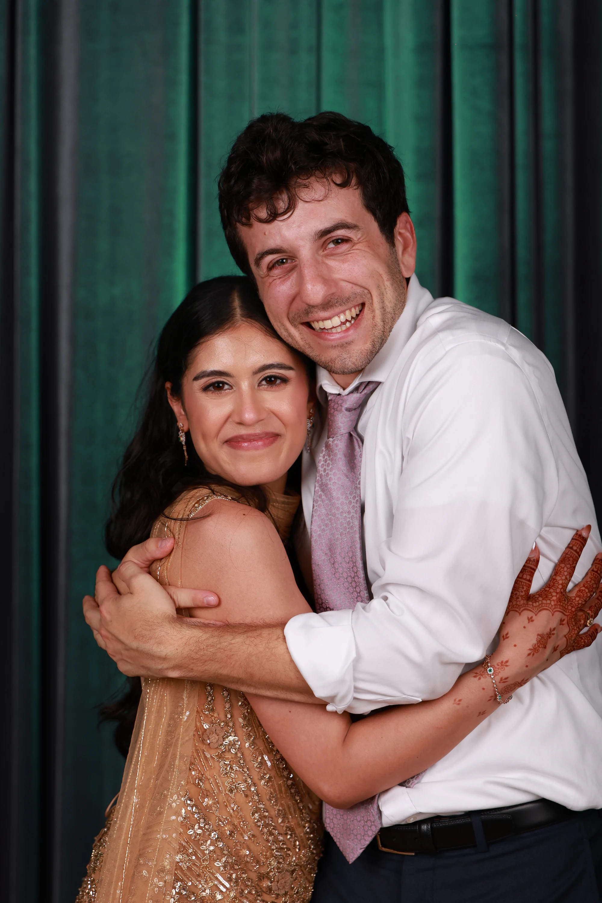 Couple wrapped in a hug, henna on her hands, green wash behind at Puja + Curtis at State Savings Bank