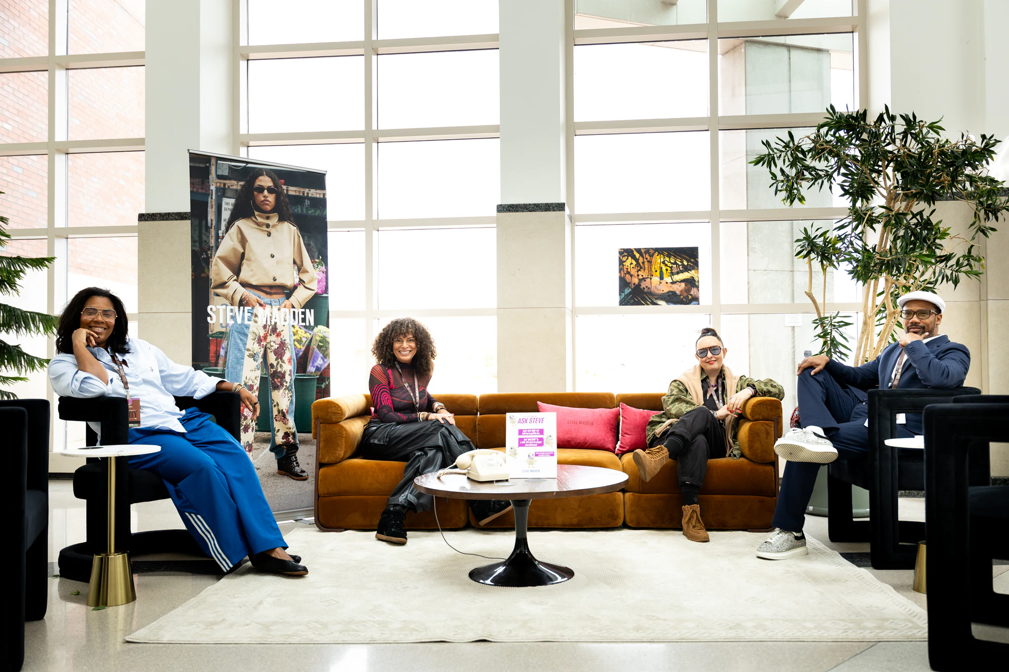 Four people seated around an orange sofa under a Steve Madden banner in a bright atrium at Black Footwear Forum