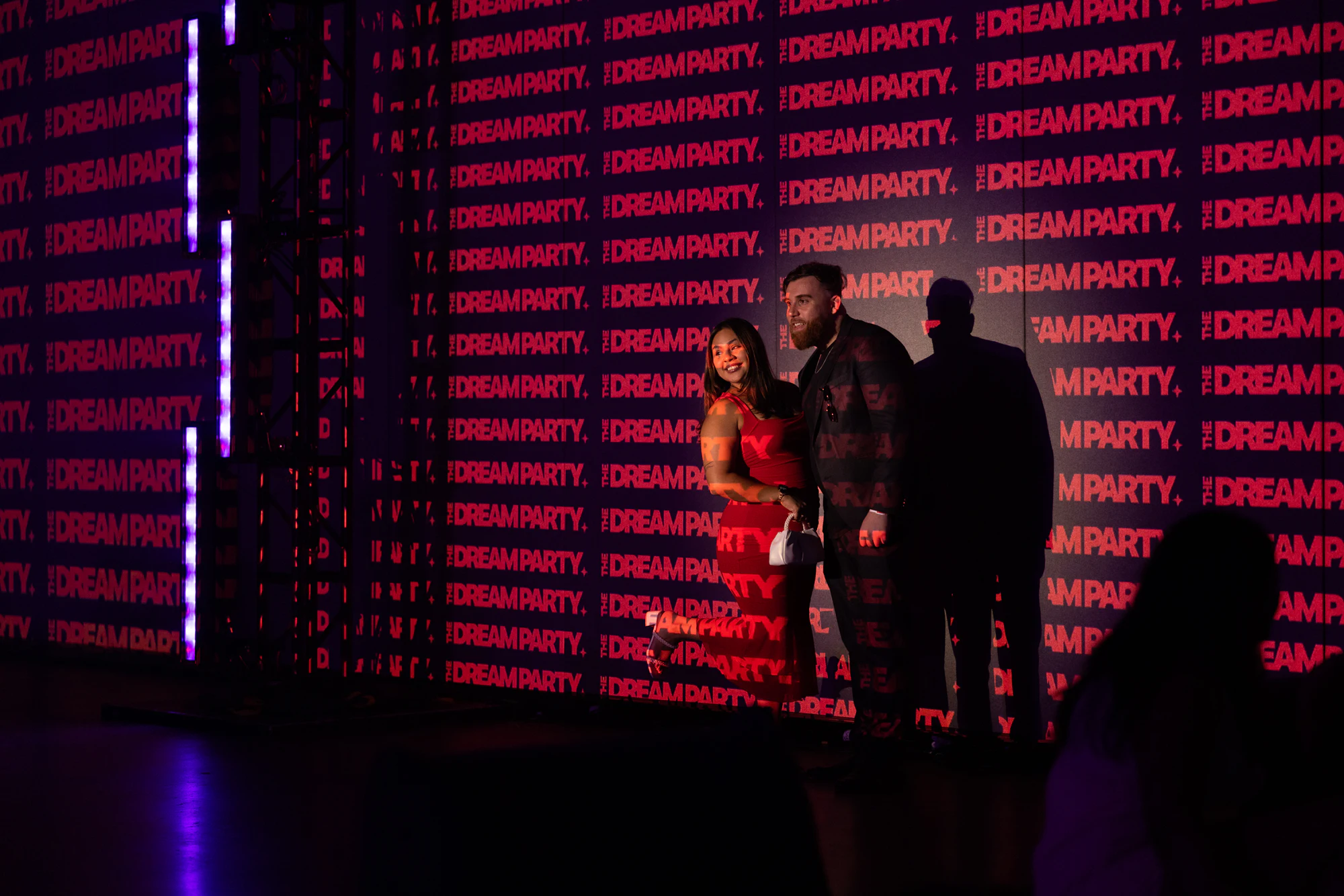 A couple posing against the red DREAMPARTY projection wall, their shadows beside them at The Dream Party: Rocket at 40