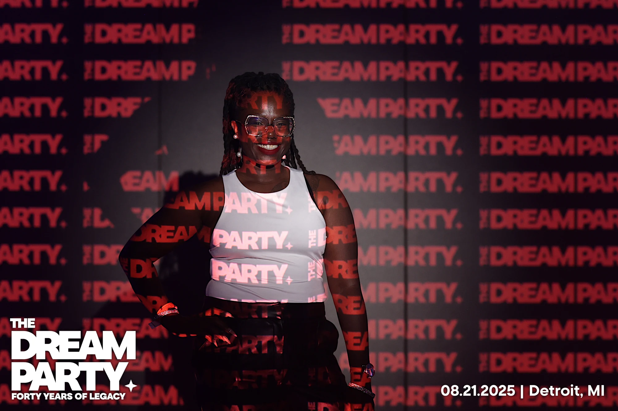 A guest in a white tank top and glasses smiling, red DREAMPARTY lettering projected across her at The Dream Party: Rocket at 40