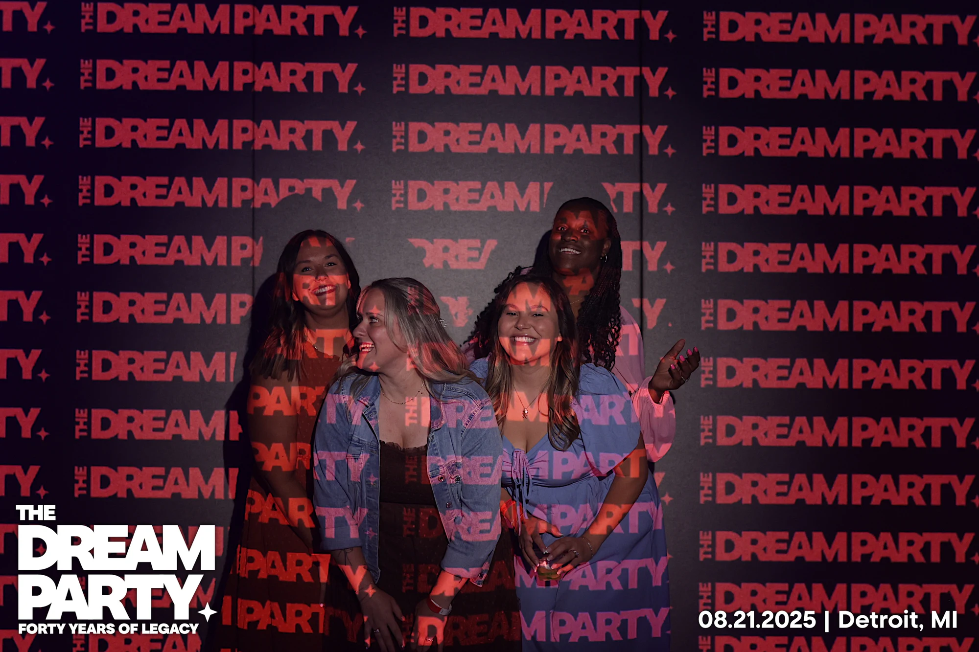 Four friends laughing under the projected red lettering, two in denim jackets at The Dream Party: Rocket at 40