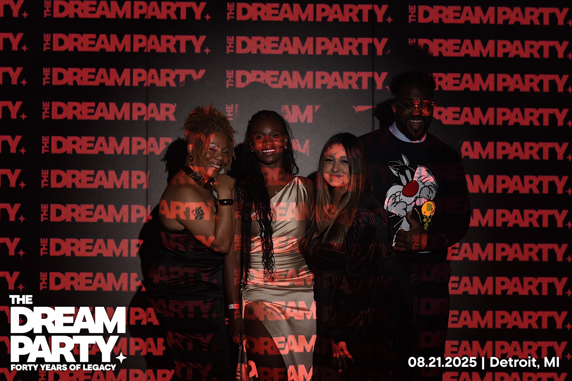 Four guests lit by the projected red lettering, one in a Sylvester the Cat sweater at The Dream Party: Rocket at 40