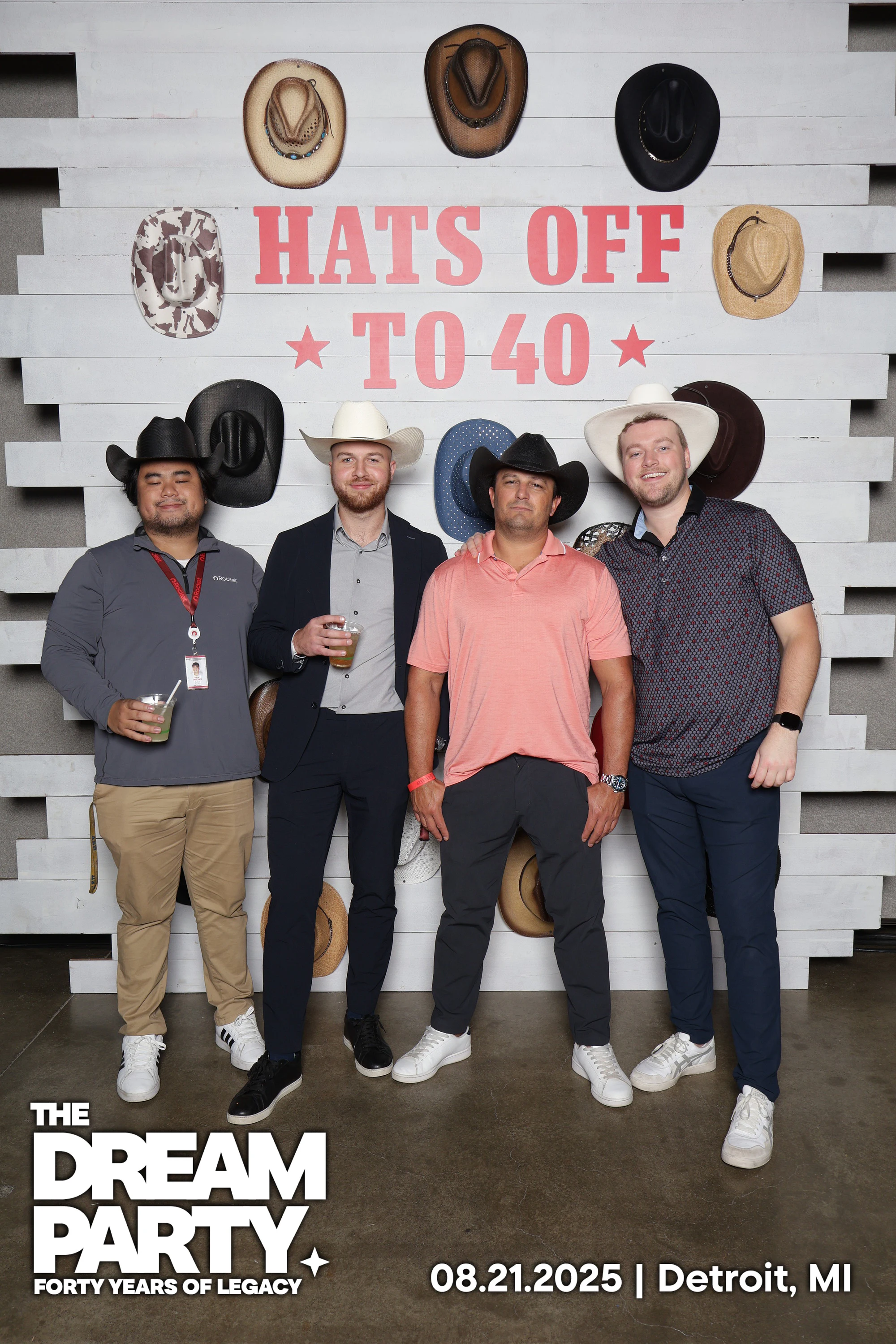 Four men in cowboy hats, two holding drinks, at the Hats Off to 40 wall at The Dream Party: Rocket at 40