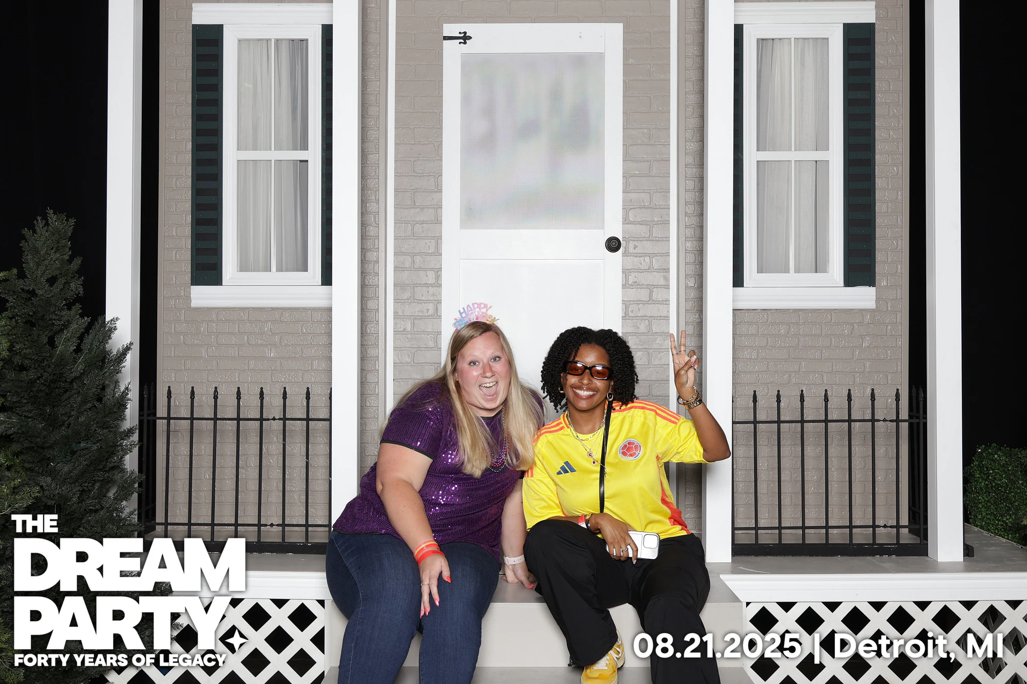 Two friends sitting on the front stoop of the brick house set, one flashing a peace sign at The Dream Party: Rocket at 40