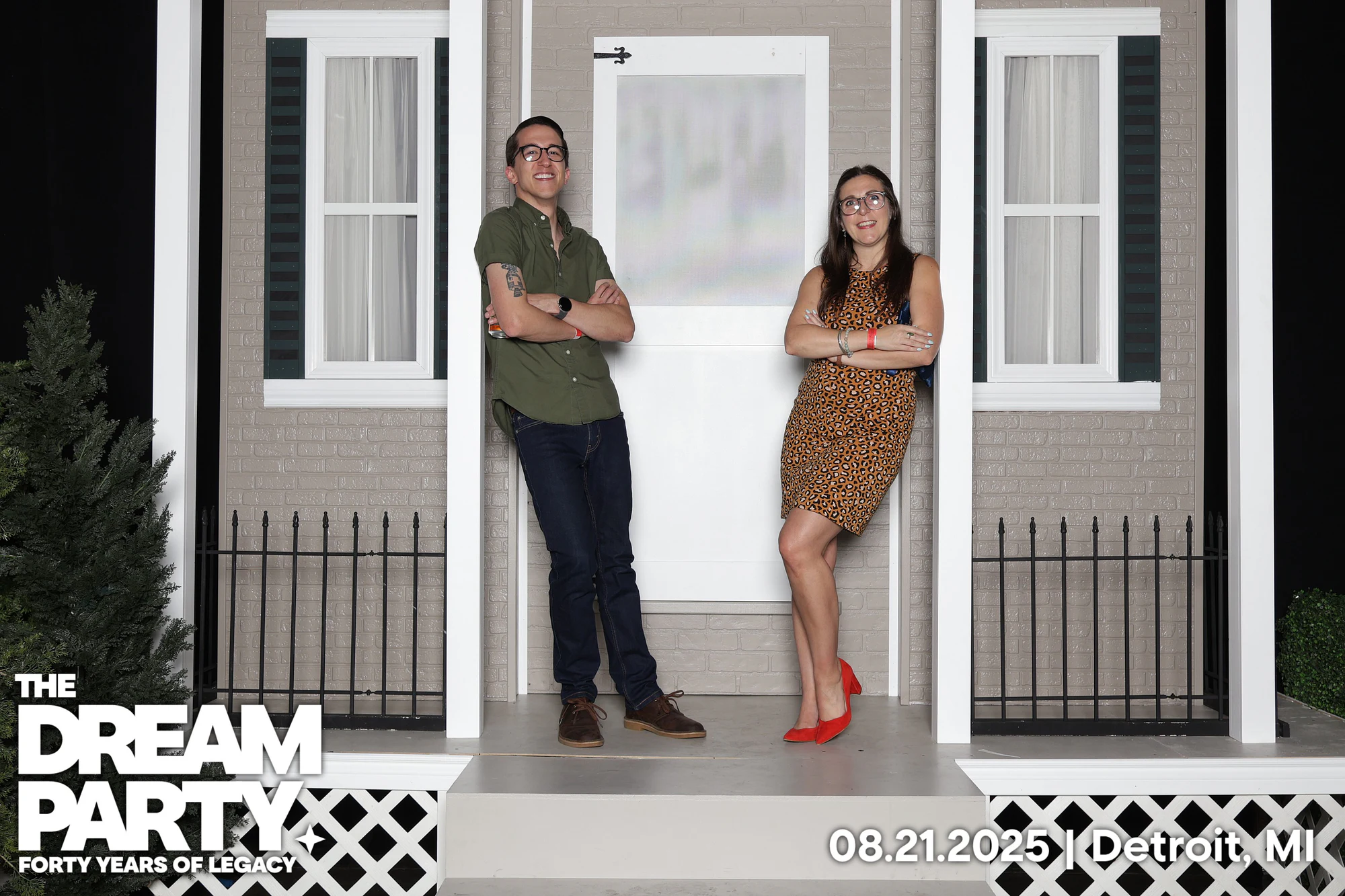 A couple leaning on the porch posts of the brick house set, arms crossed at The Dream Party: Rocket at 40