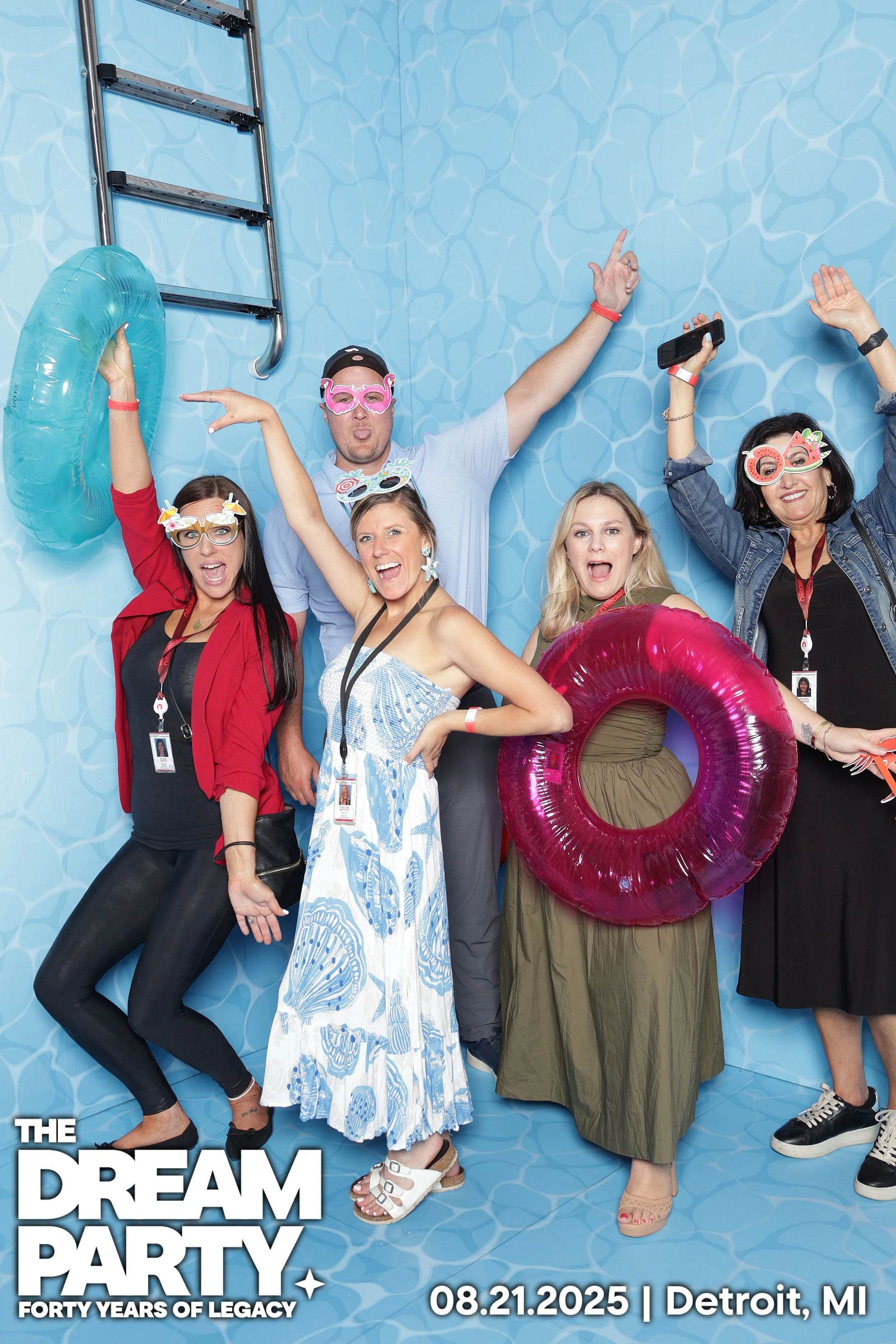 Five coworkers in novelty glasses cheering in the pool set, one holding a pink inner tube at The Dream Party: Rocket at 40