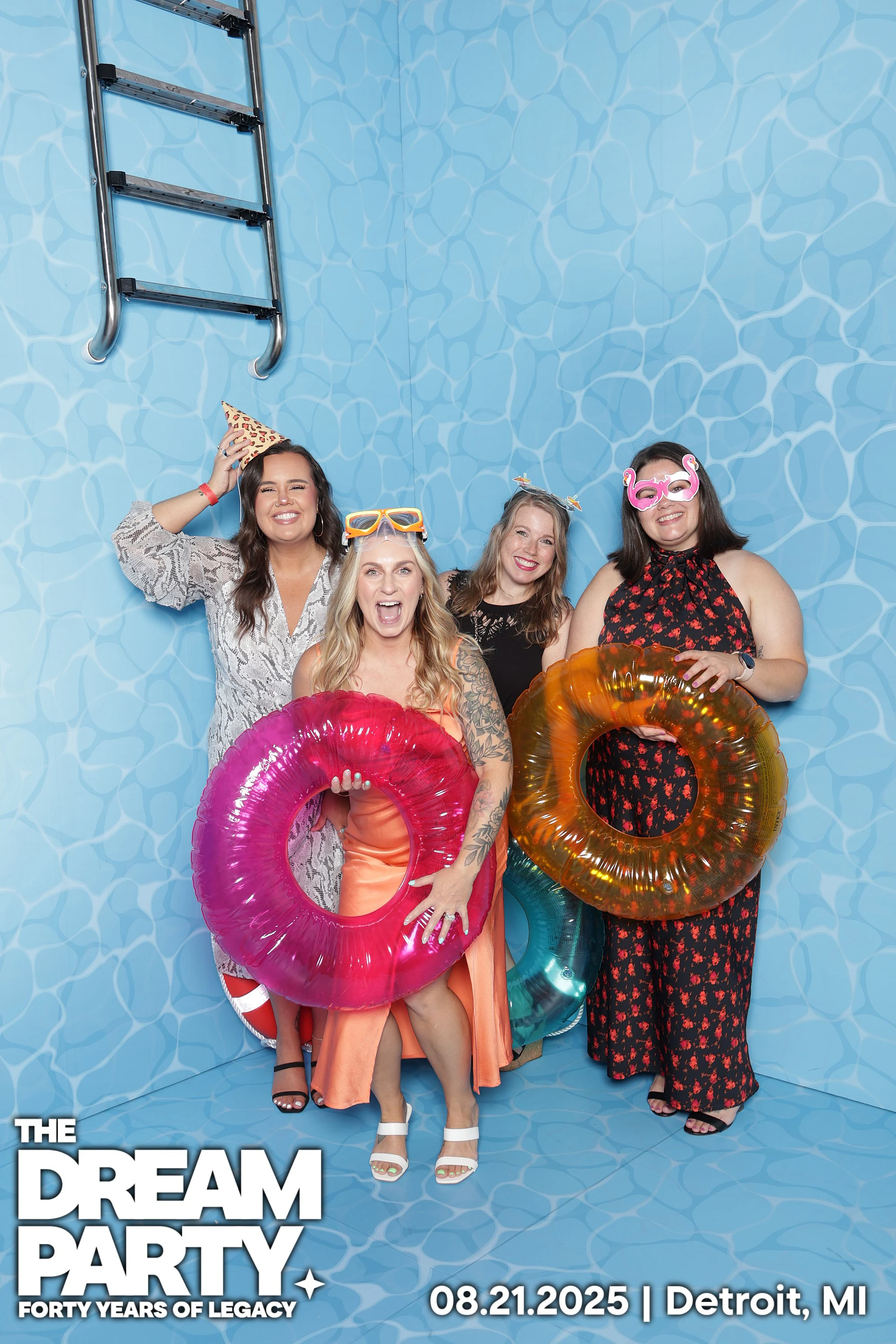 Four friends with pink and orange inner tubes in the pool set, one in swim goggles at The Dream Party: Rocket at 40