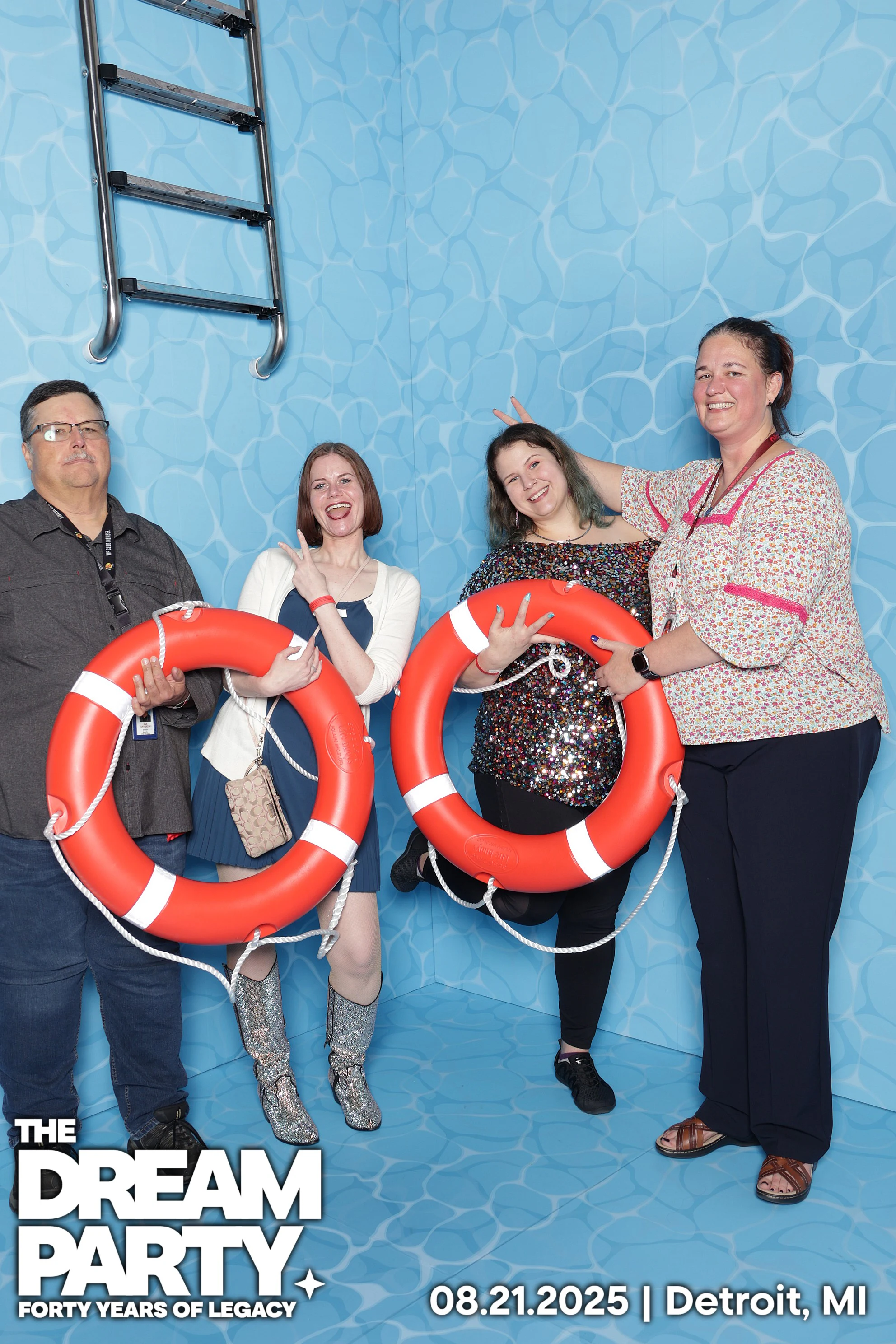 Four coworkers holding orange life rings in the pool set, two giving bunny ears at The Dream Party: Rocket at 40