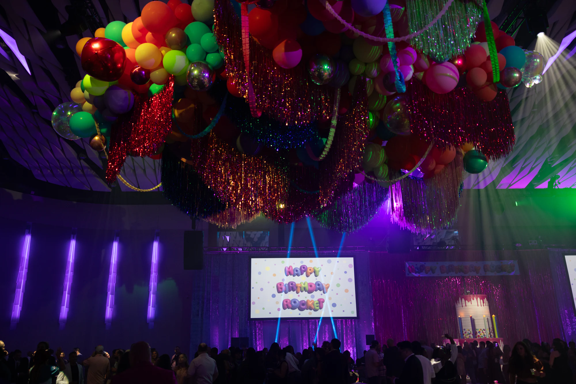 A balloon and tinsel installation over the crowd, Happy Birthday Rocket on the screen at The Dream Party: Rocket at 40