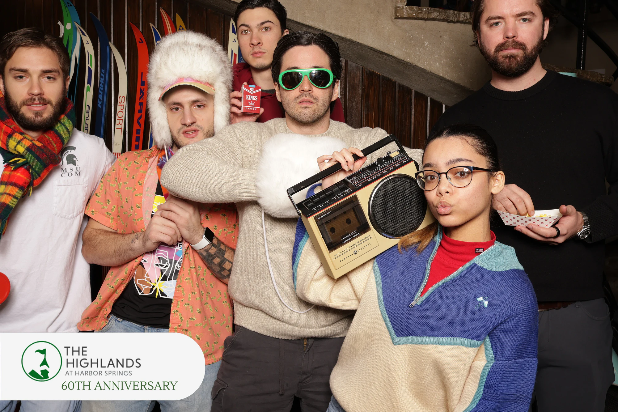 Six friends in retro ski sweaters, one woman holding the boombox up by her face at The Highlands 60th Anniversary