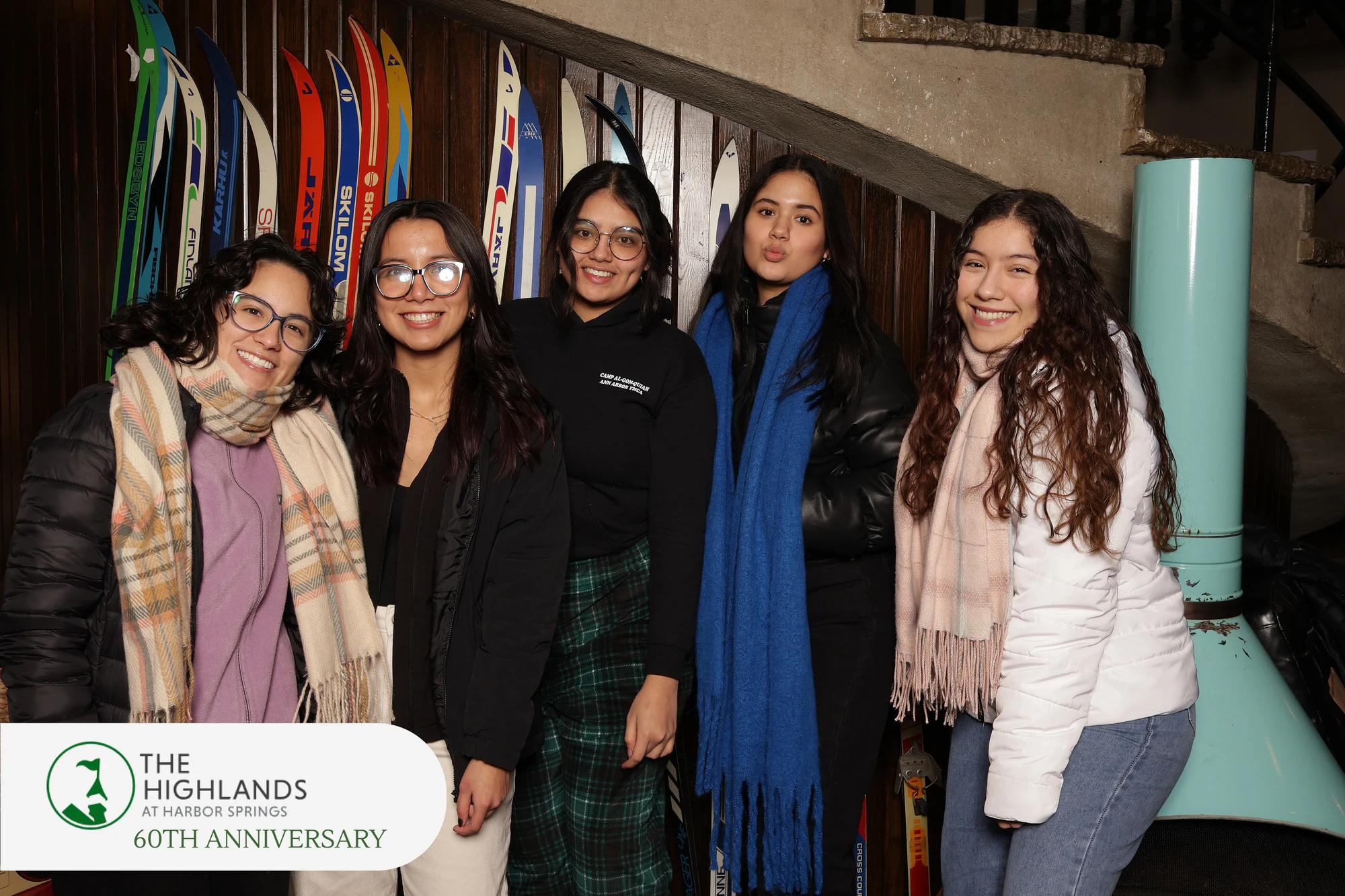 Five friends in scarves and winter coats lined up in front of the vintage ski wall at The Highlands 60th Anniversary