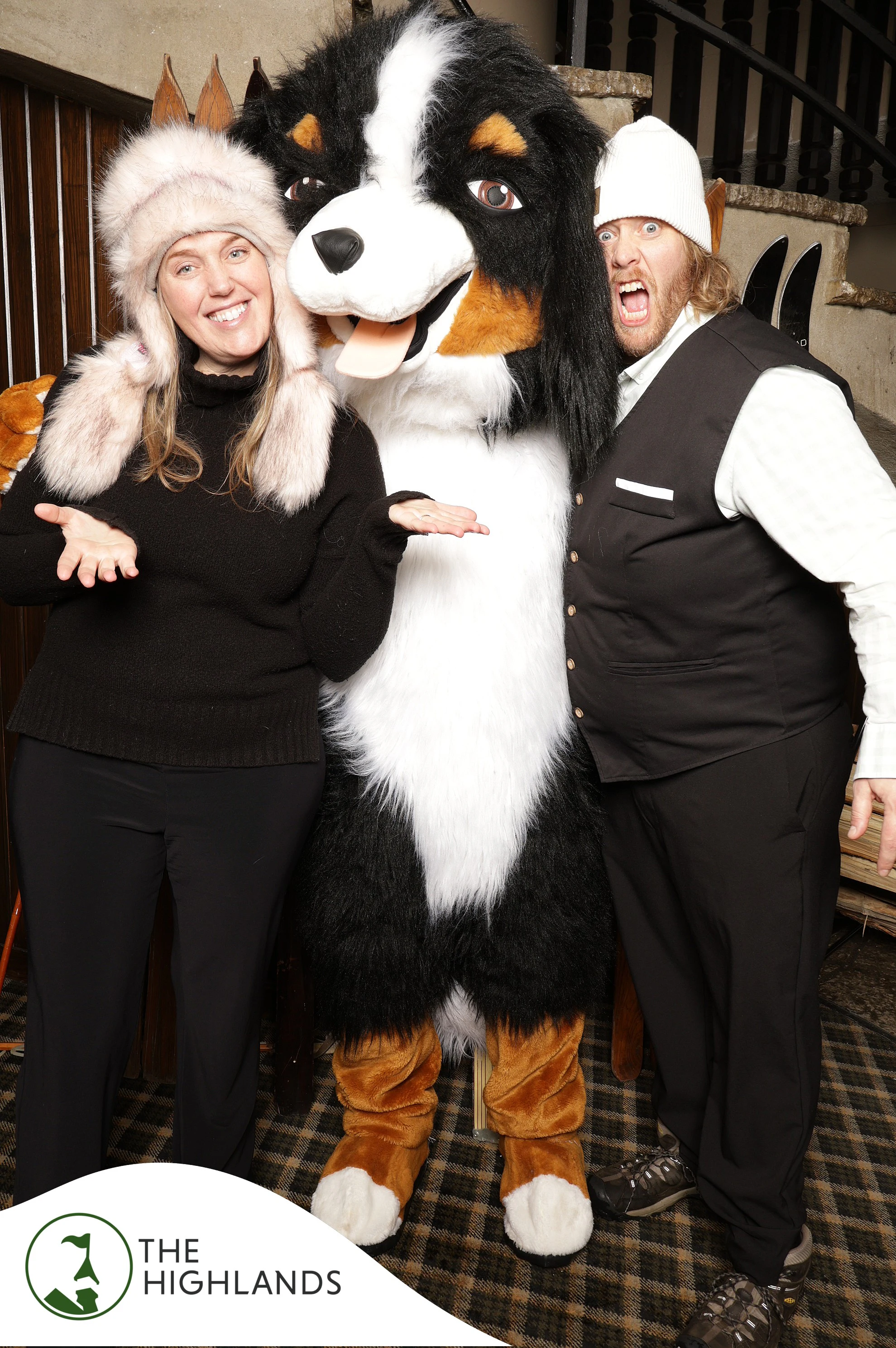A woman in a fur hat and a man in a vest on either side of a big dog mascot at The Highlands 61st Anniversary