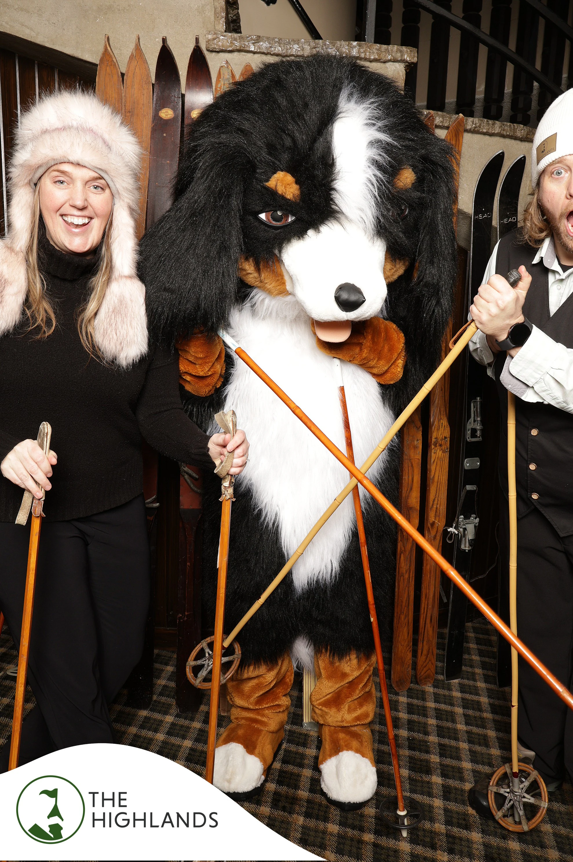 The dog mascot crossing its vintage ski poles between the woman and the man at The Highlands 61st Anniversary