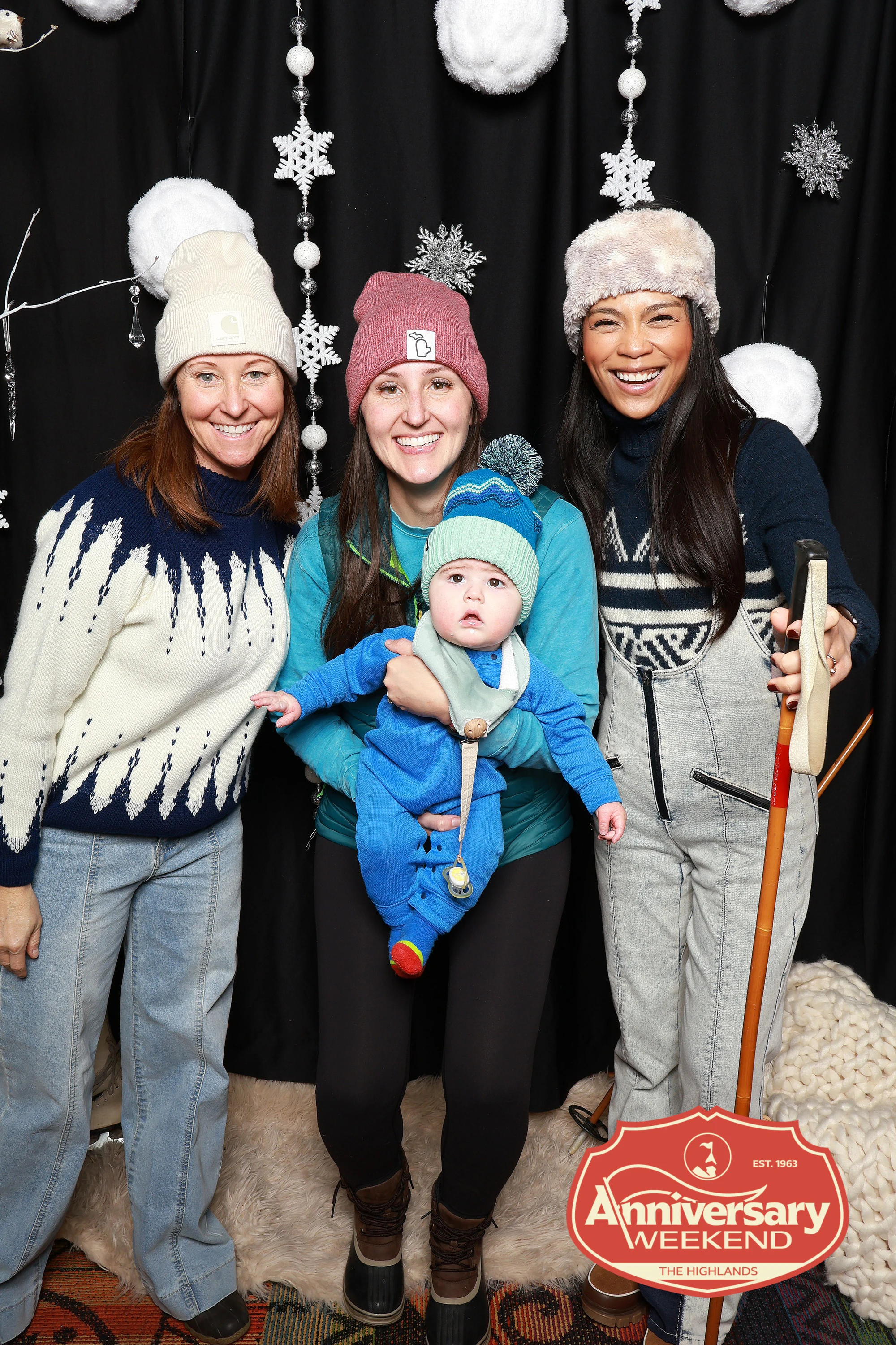 The three women smiling with the baby in the blue snowsuit at The Highlands Anniversary Weekend