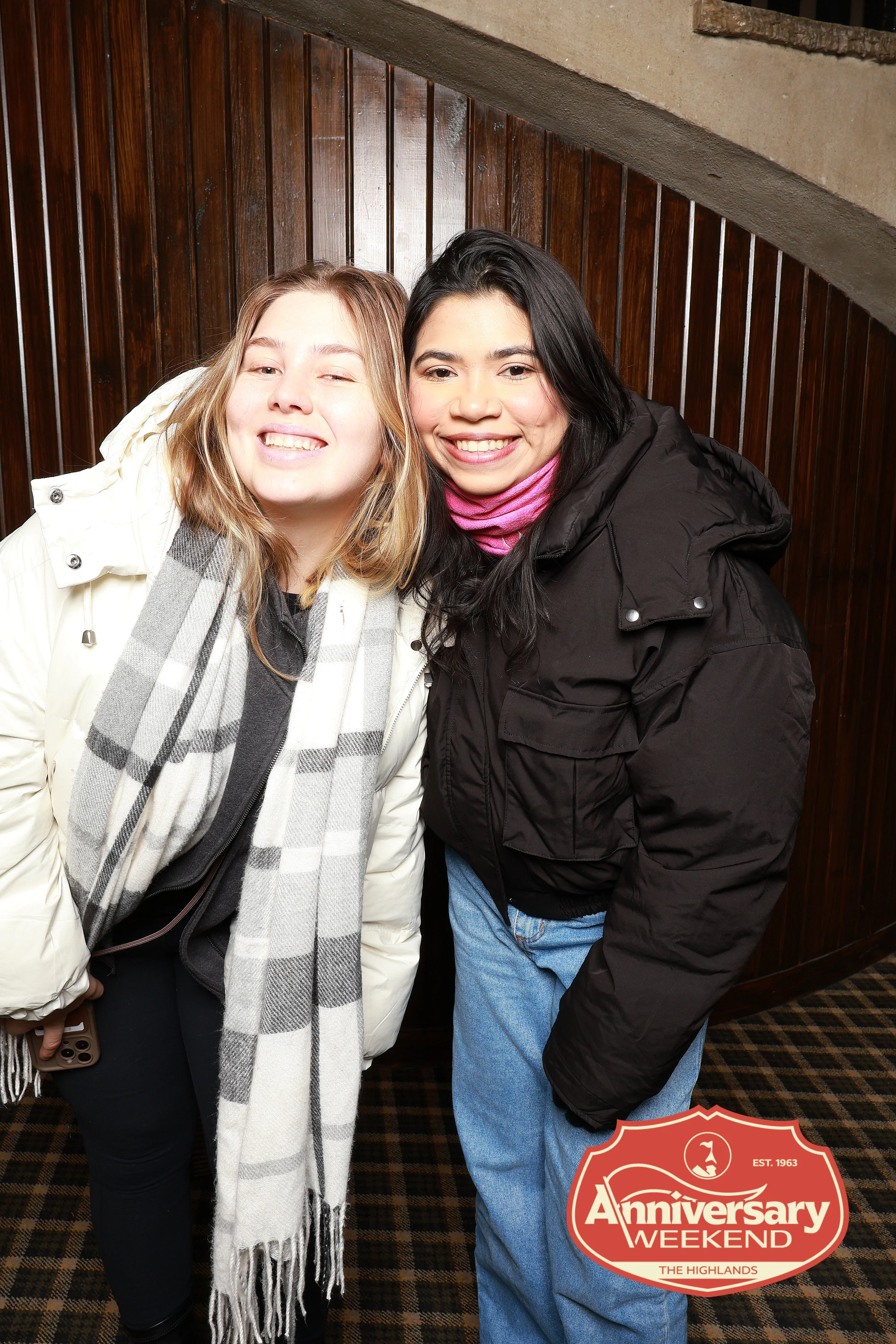 Two friends in winter coats and scarves, cheek to cheek at The Highlands Anniversary Weekend