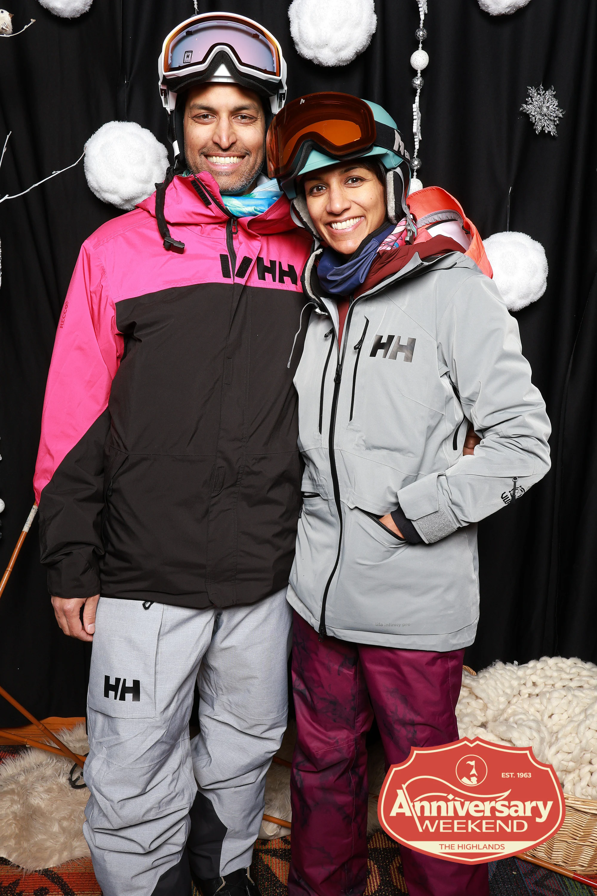 The couple in ski jackets, both in helmets and goggles, smiling at The Highlands Anniversary Weekend