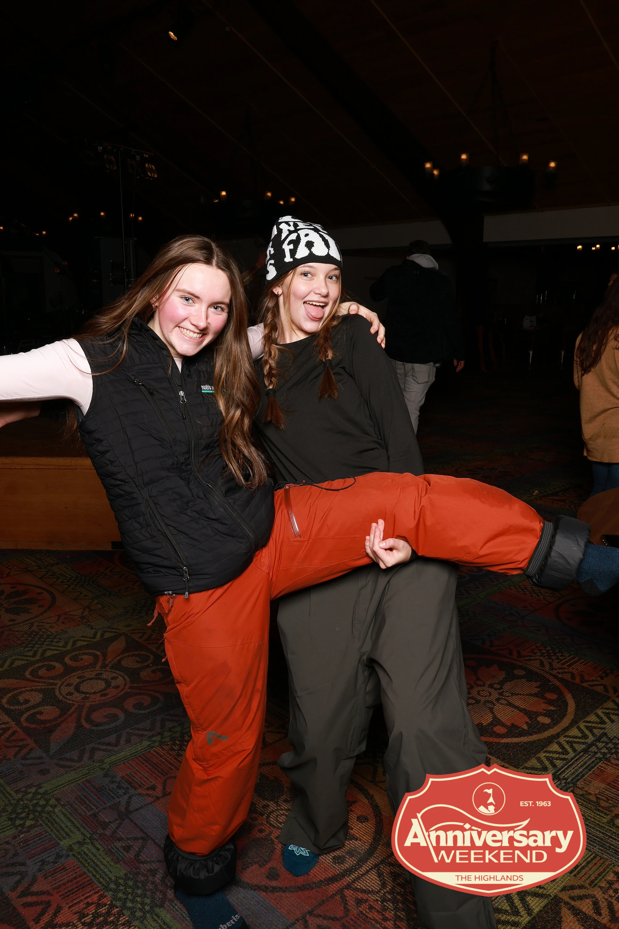 The two friends, one swinging her leg up over the other’s at The Highlands Anniversary Weekend