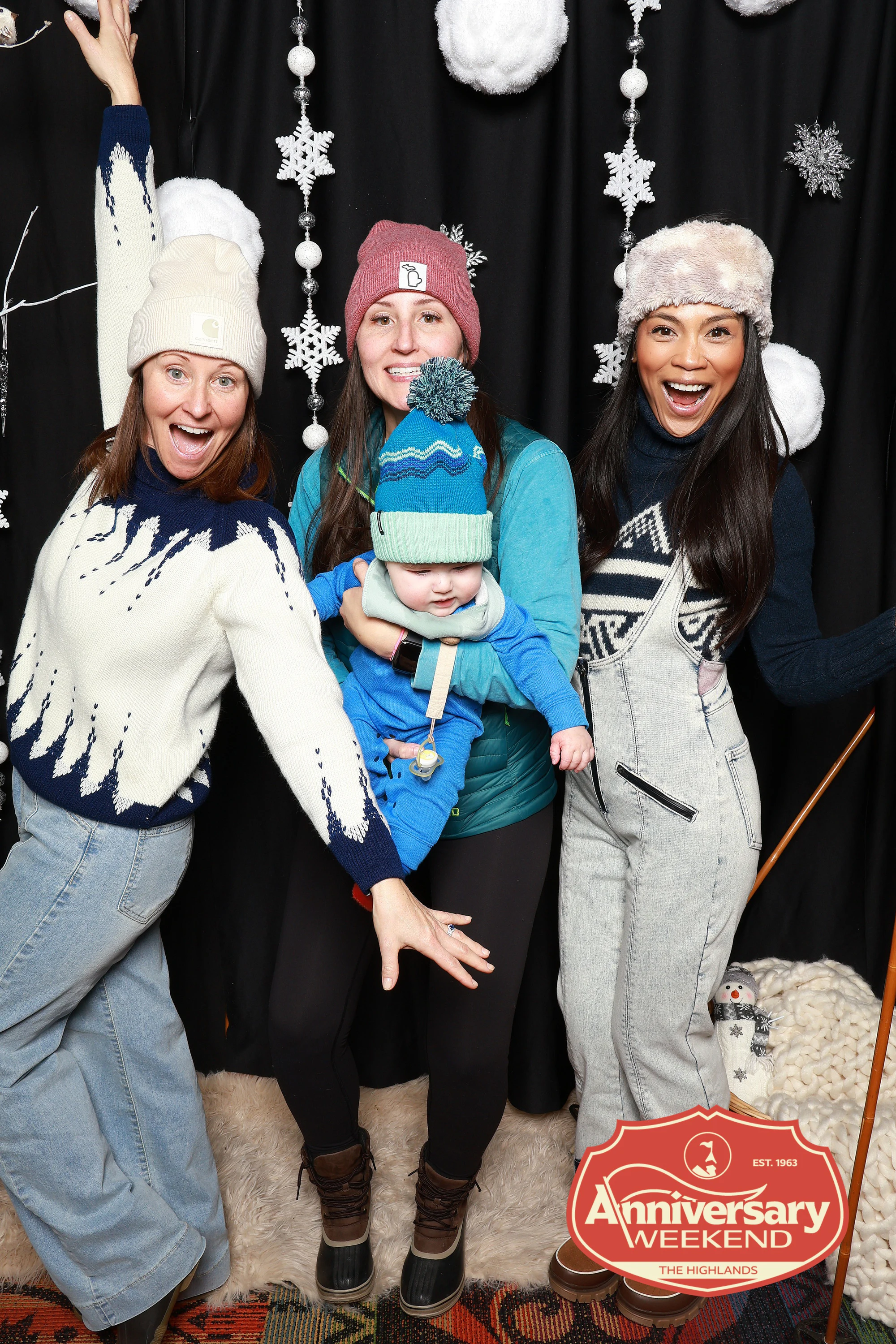Four adults and a baby, one arm thrown up, snowflake backdrop behind at The Highlands Anniversary Weekend